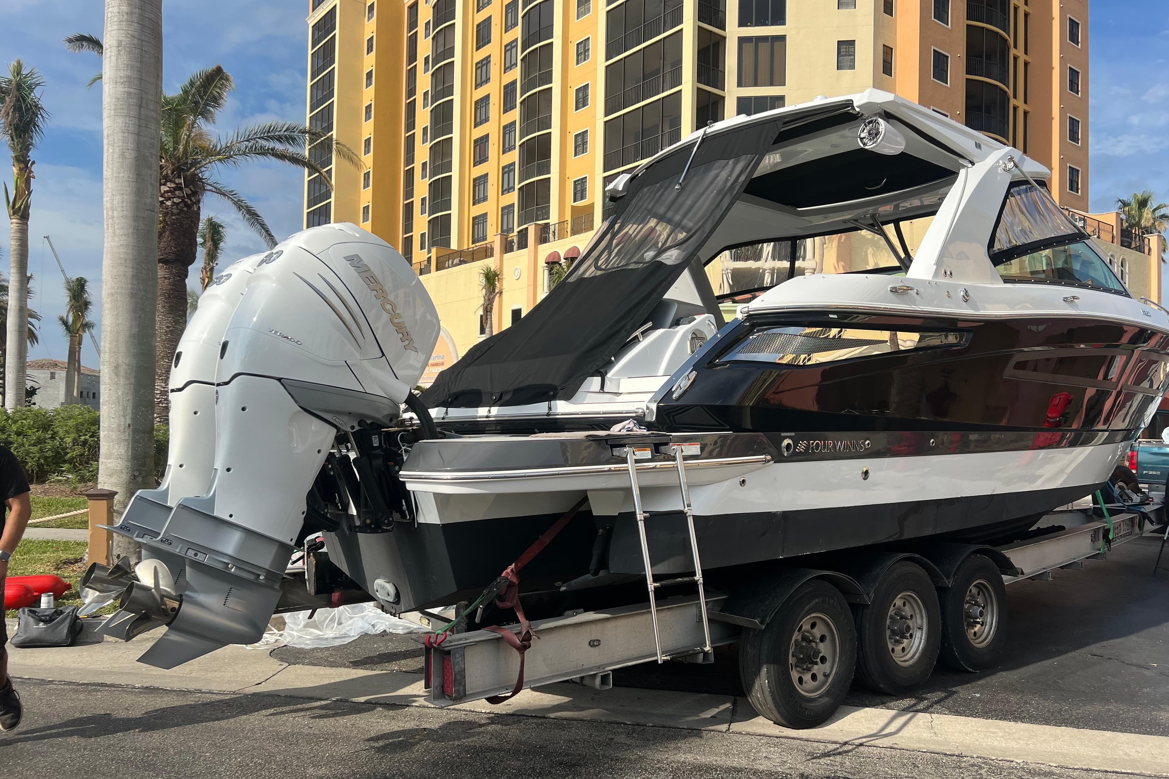 2023 Four Winns H350 OB boat on trailer near tall building and palm trees.