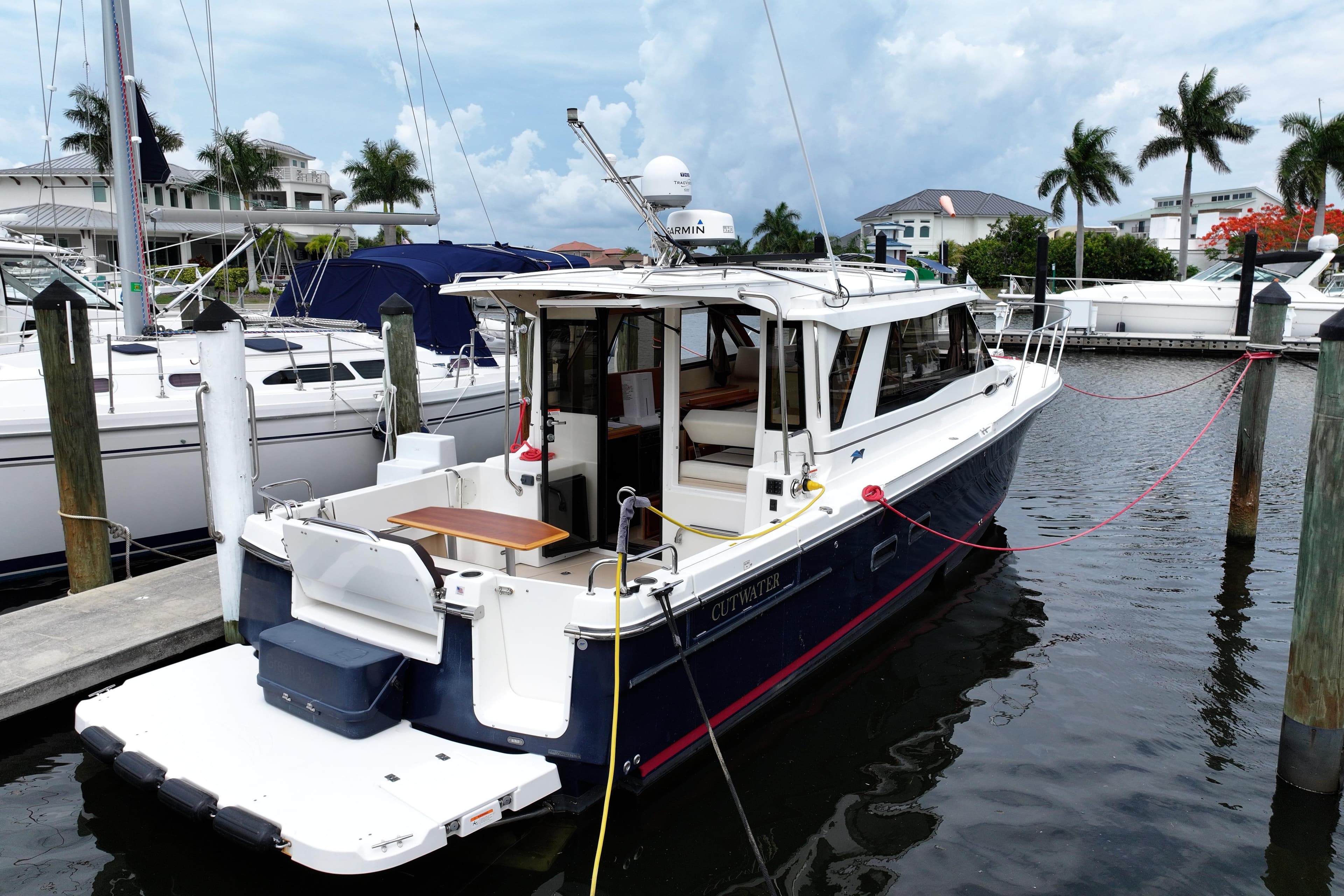 2015 Cutwater 30 Sedan docked at marina, surrounded by palm trees and luxury boats.