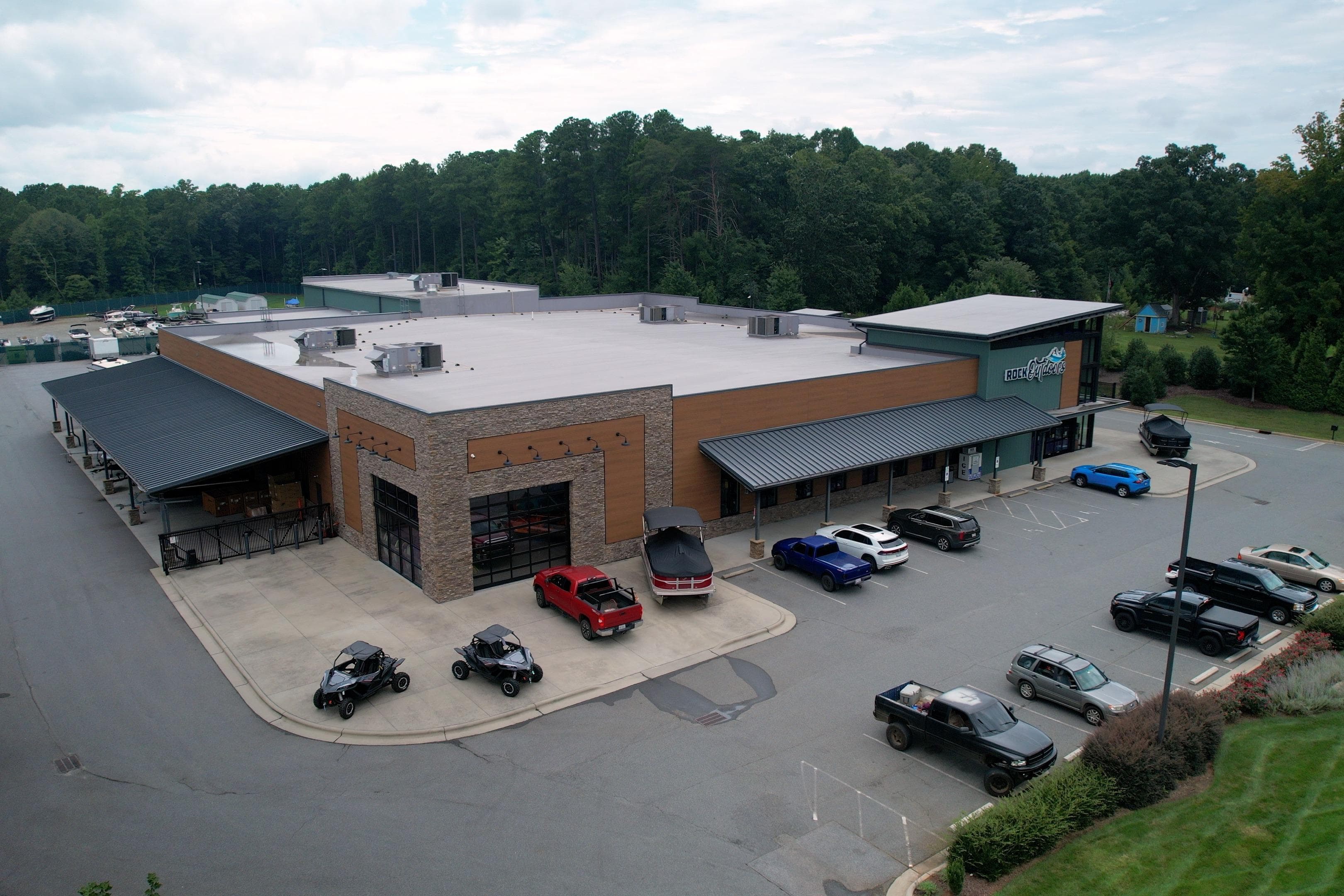 Aerial view of a commercial building with parked vehicles, surrounded by trees.