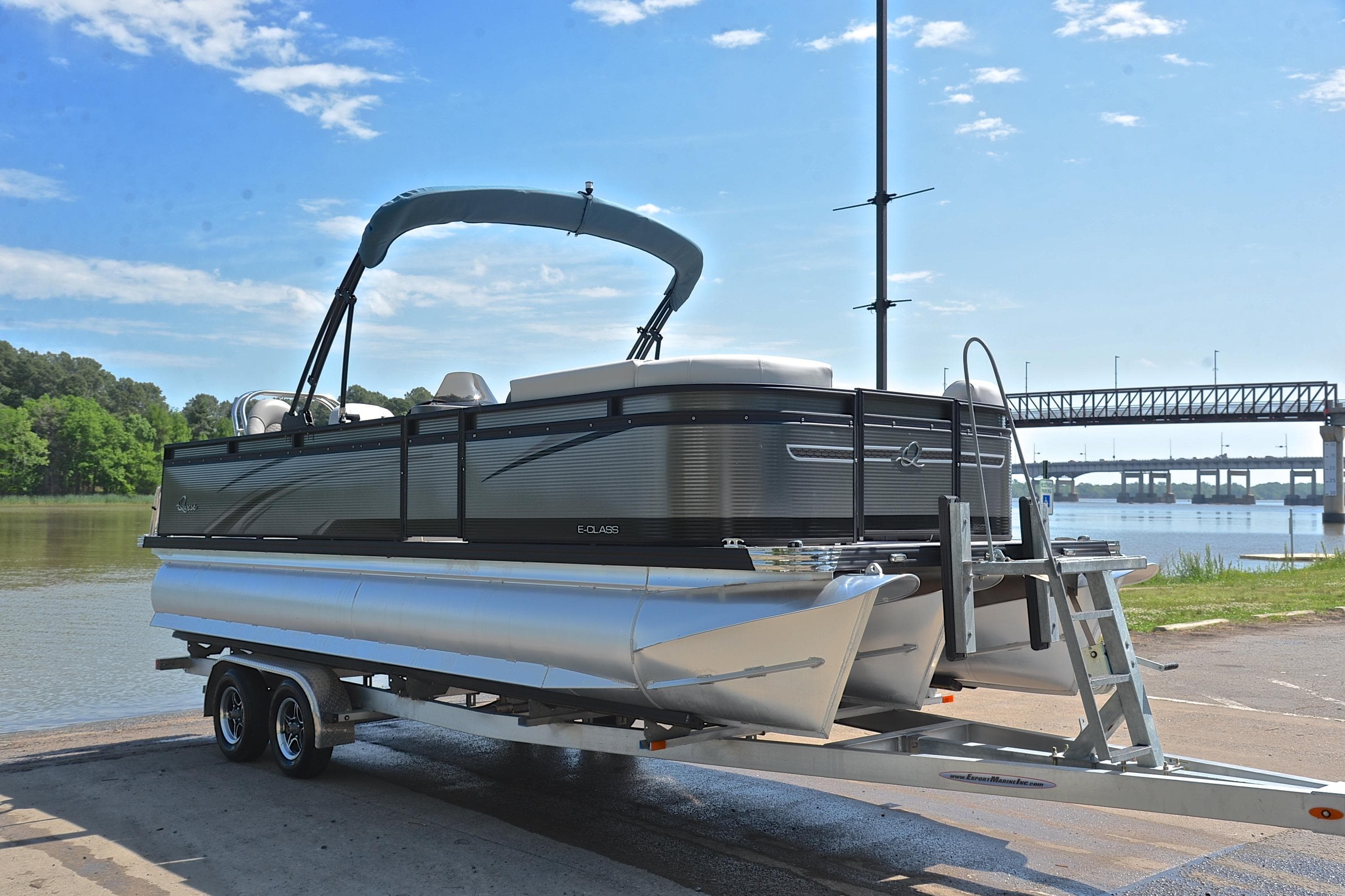 2022 Qwest E822 pontoon boat on trailer by a river with bridge in background.