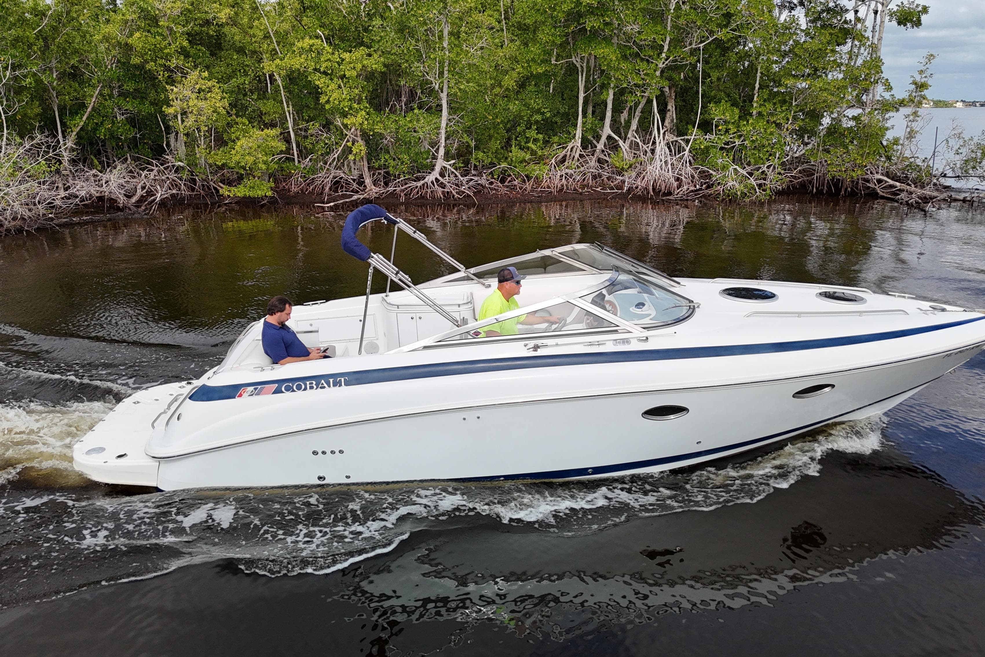 1999 Cobalt 293 boat cruising on a river with lush green trees in the background.