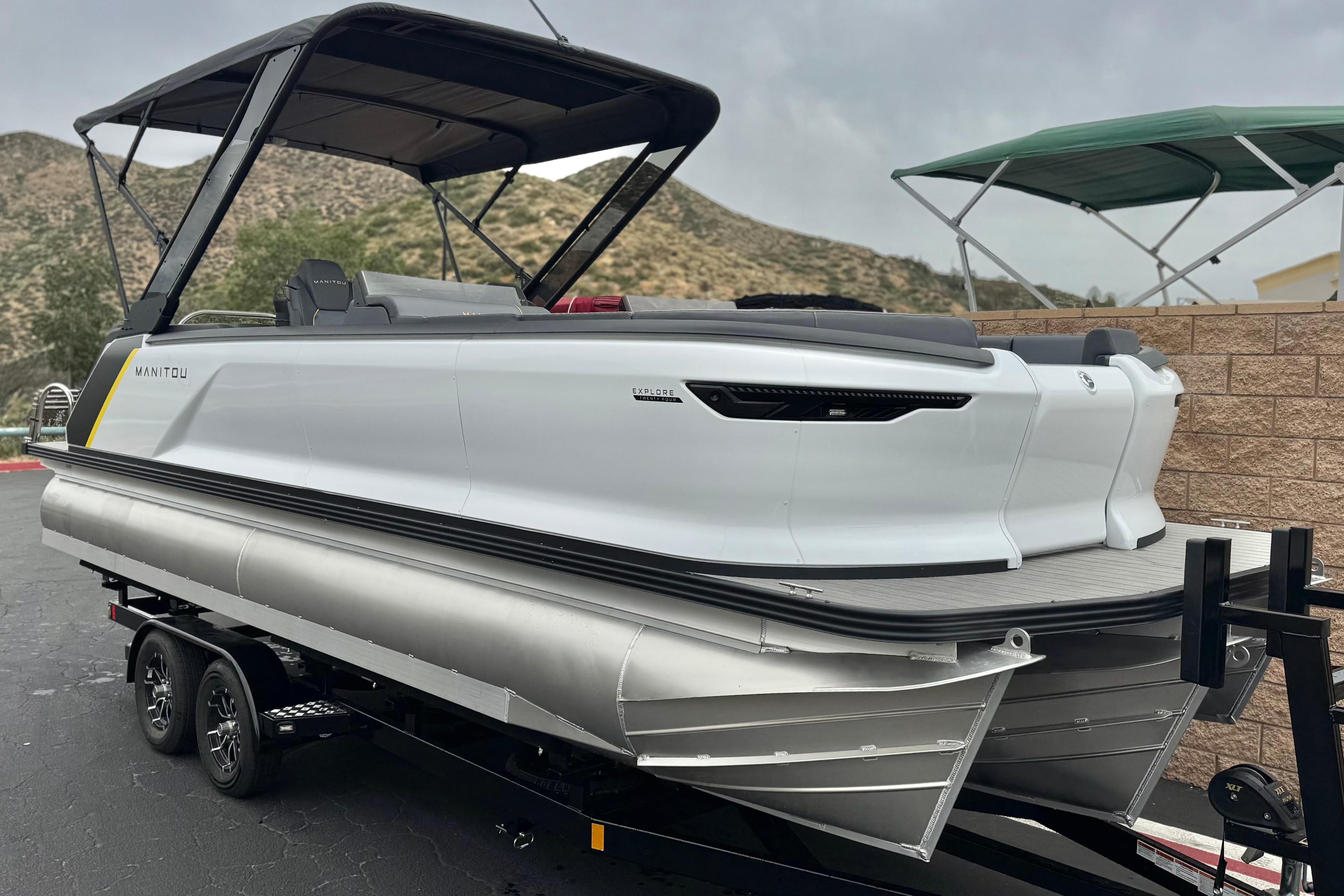 2025 Manitou EXPLORE 24 pontoon boat on trailer, sleek design, mountainous backdrop.
