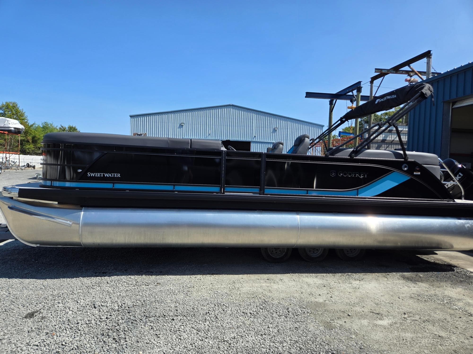 2025 Godfrey Sweetwater 2486 SB pontoon boat, black and blue, parked outdoors.