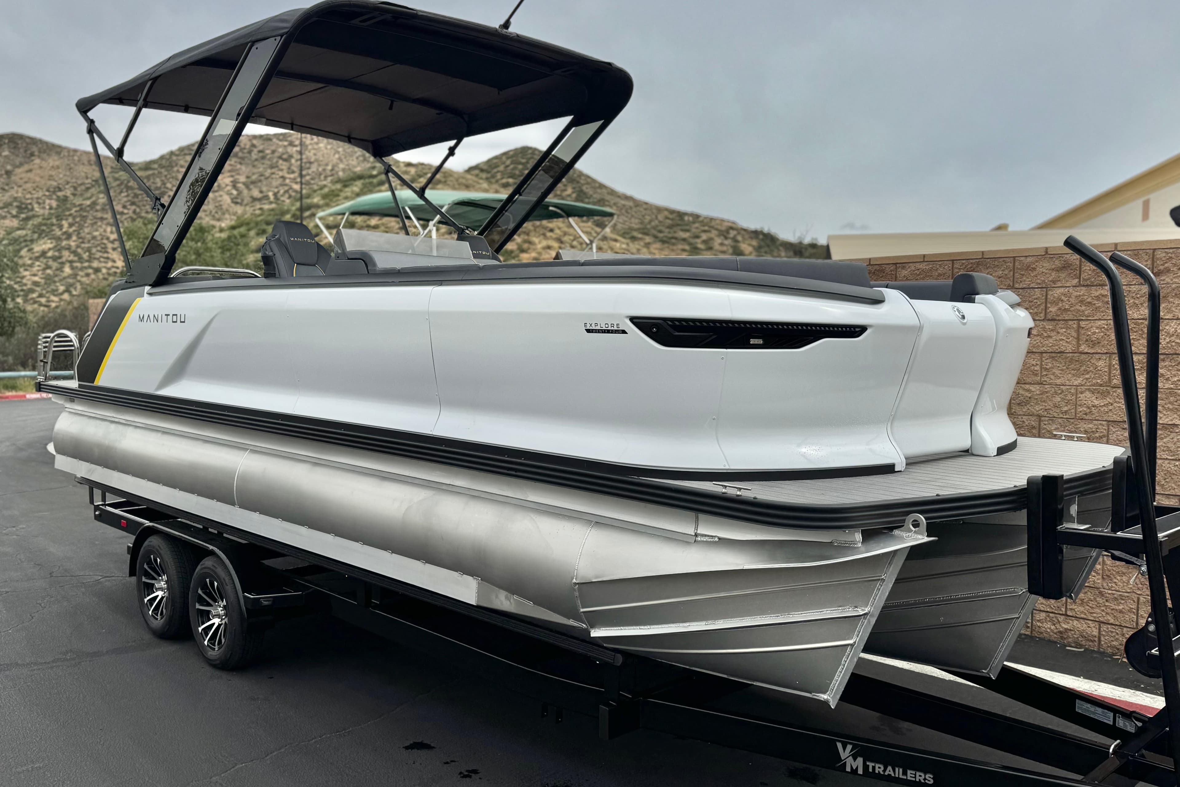 2025 Manitou EXPLORE 24 pontoon boat on trailer, sleek design, parked outdoors.