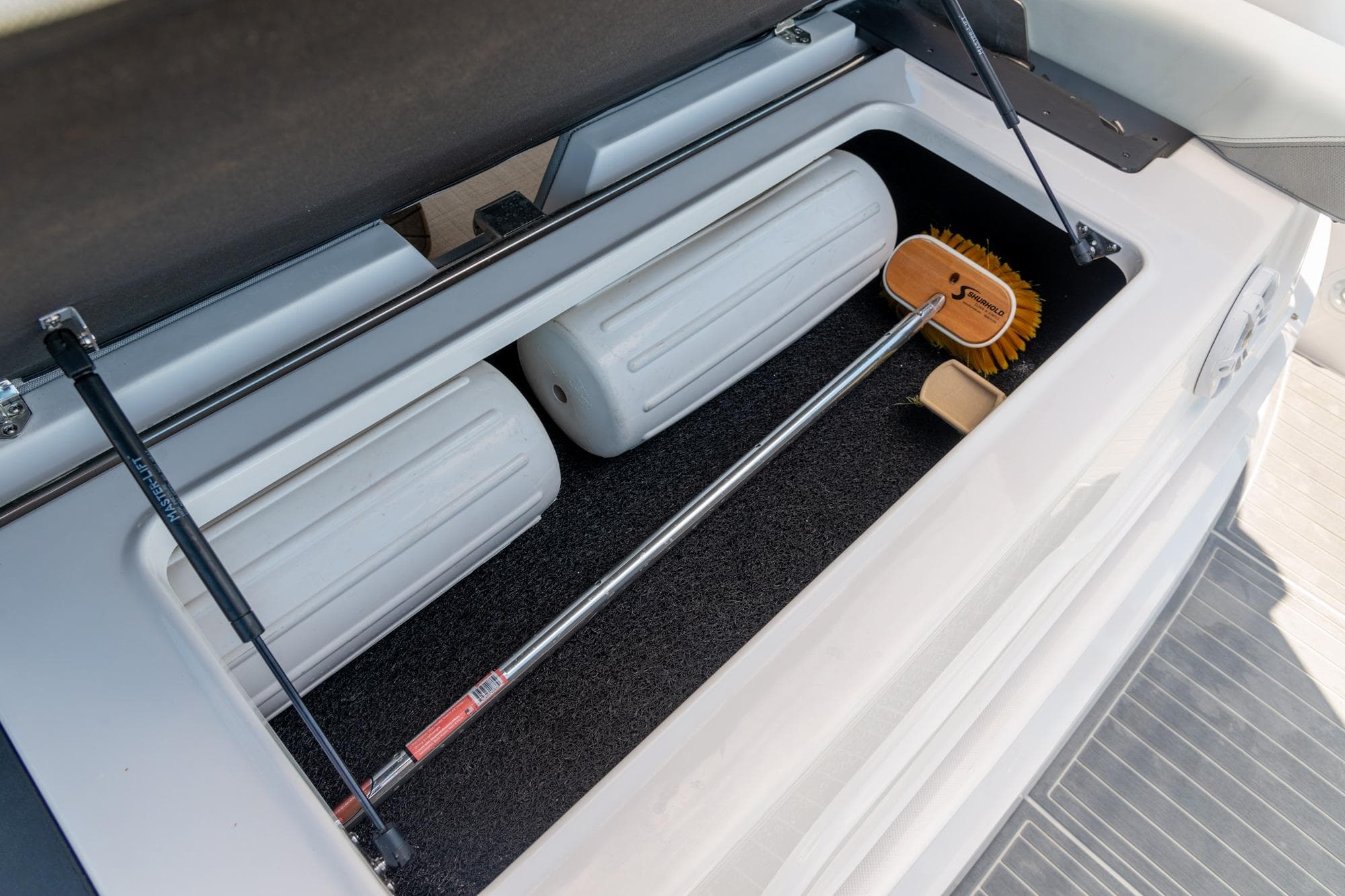 Storage compartment on 2026 Regal 36 XO boat with fenders and cleaning brush.