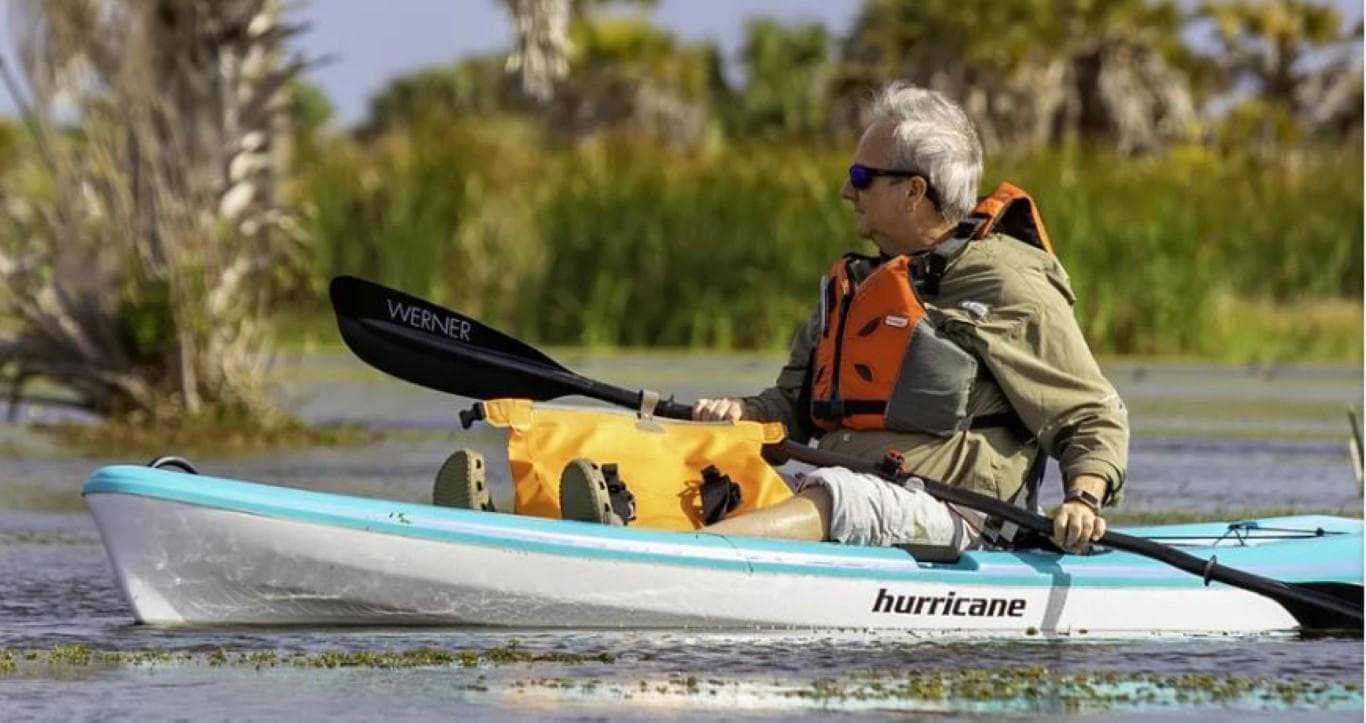 Man kayaking in a 2023 Hurricane Kayaks Skimmer 106 on a calm lake.