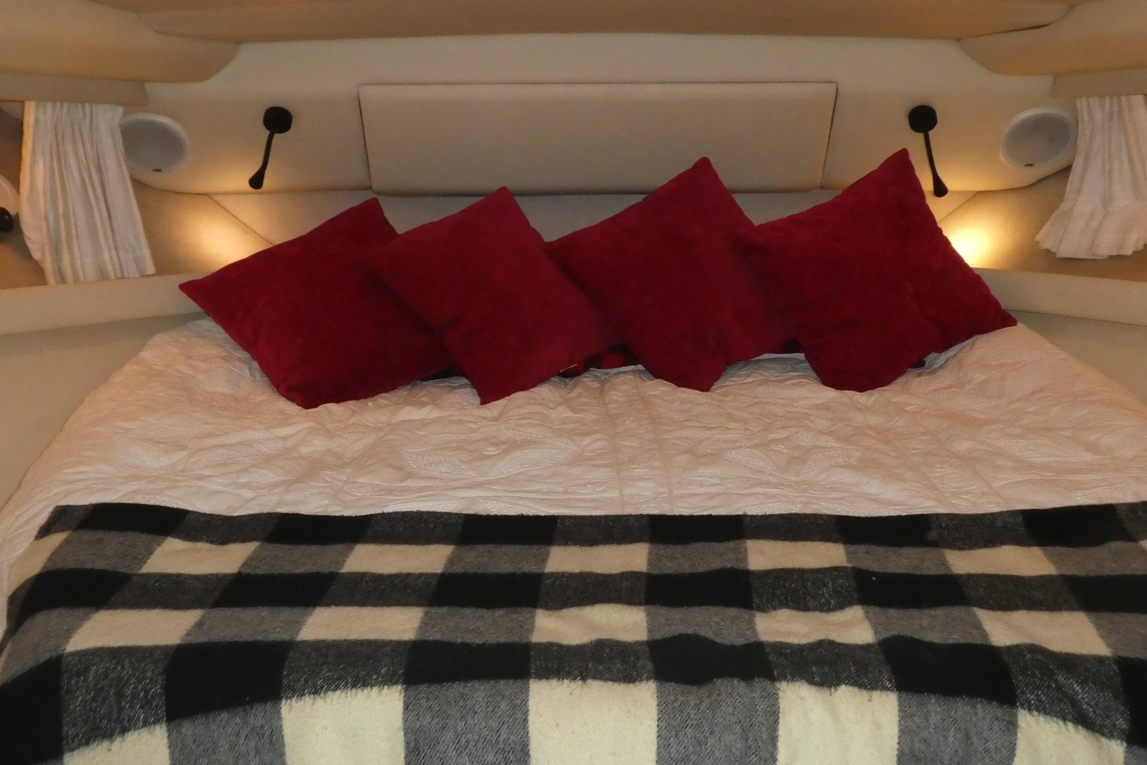 Cozy bedroom in 1994 Bayliner 4388 Motor Yacht with red pillows and plaid blanket.
