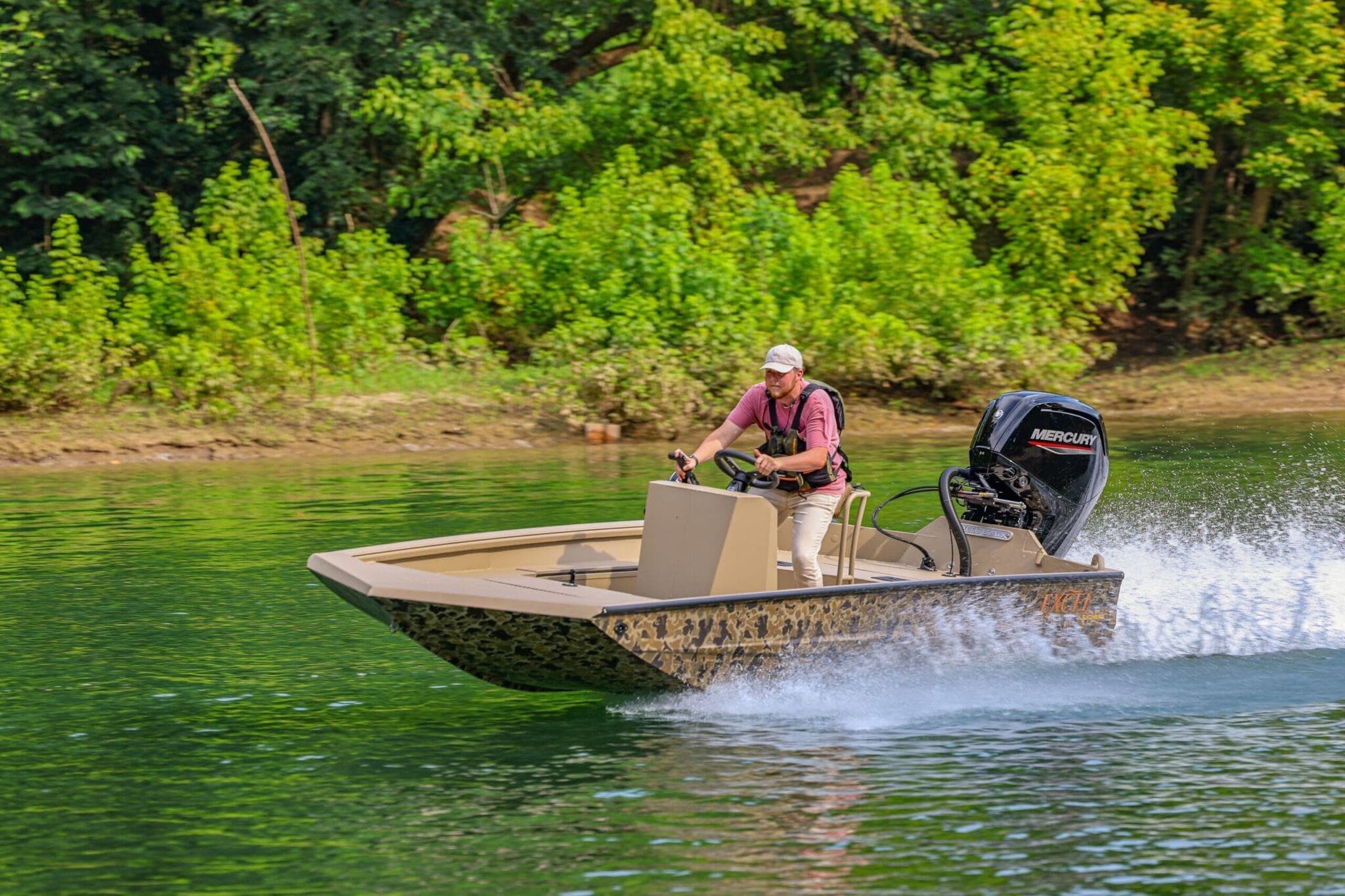 2026 Excel Switchblade boat speeding on a lake with lush green trees in the background.
