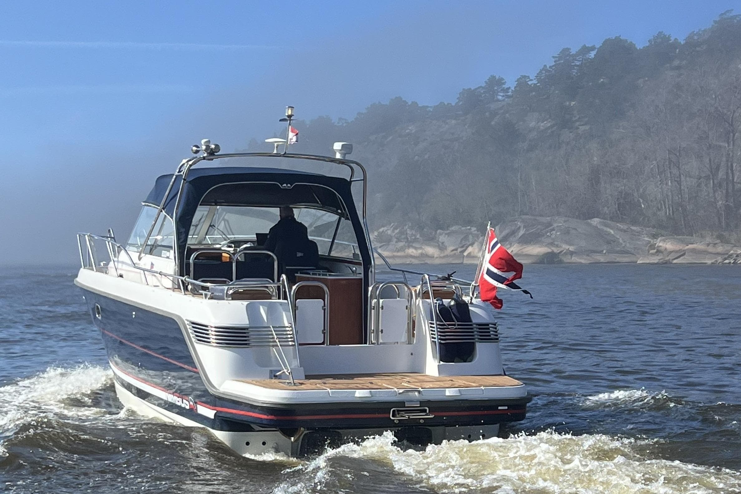 Nimbus 35 Nova 2005 motorboat cruising on a misty lake with rocky shoreline.