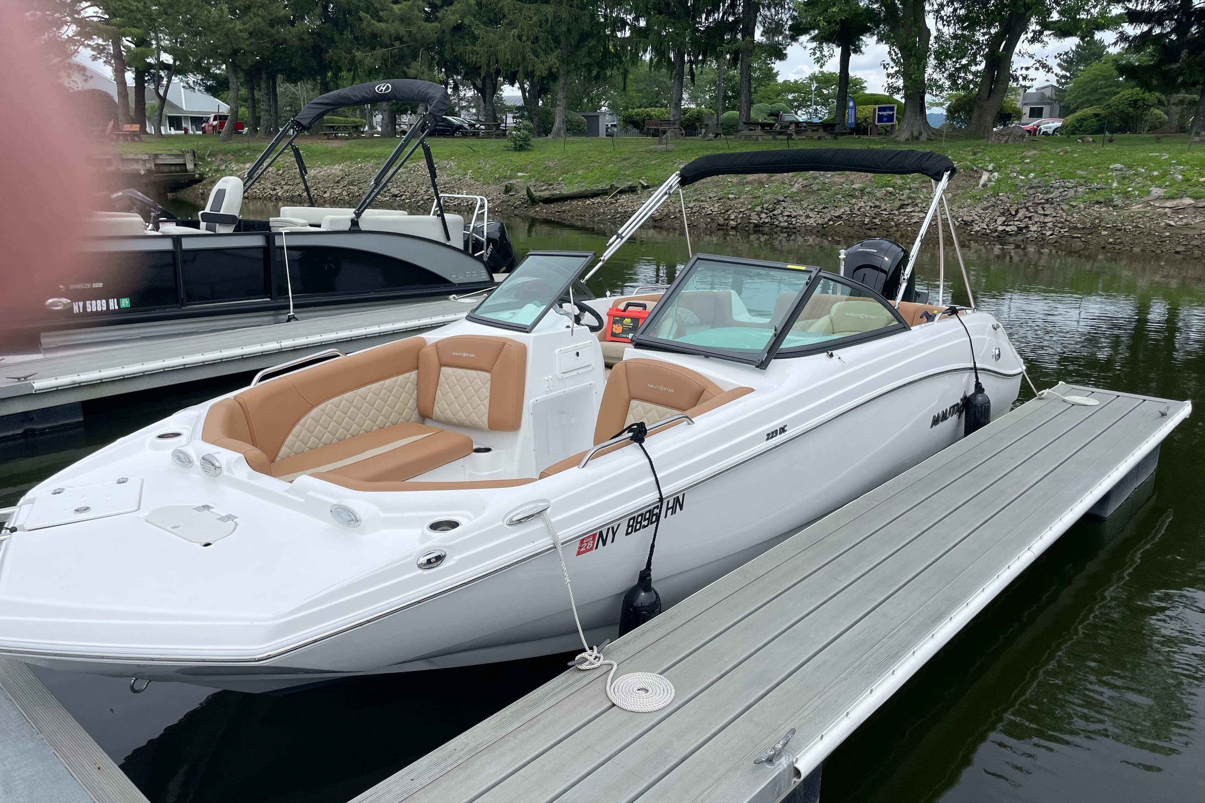 2025 NauticStar 223 DC Deck boat docked, featuring tan seating and sleek design.