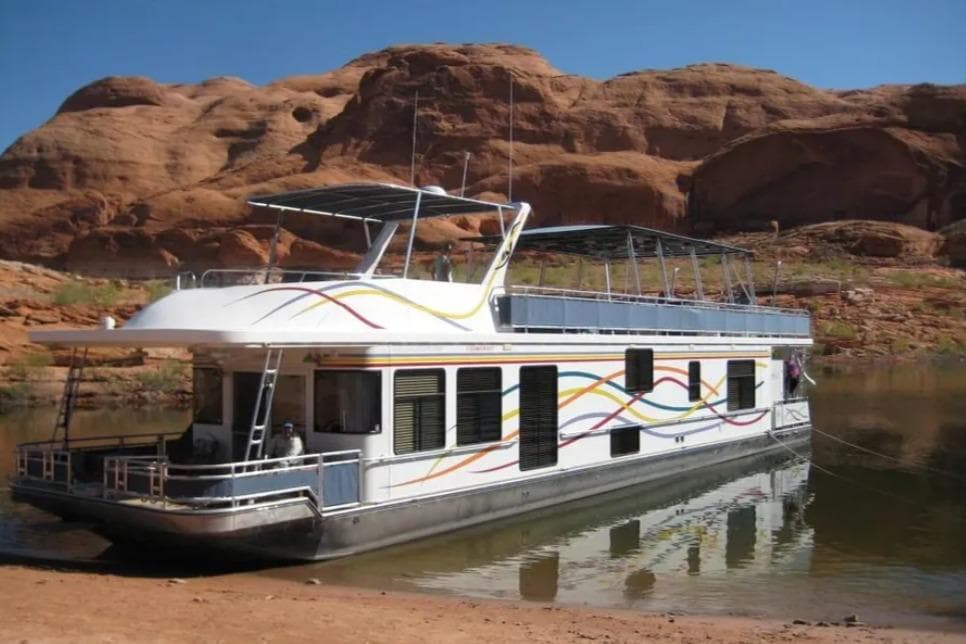 2005 Sumerset Star Chaser houseboat docked by red rock cliffs under clear blue sky.