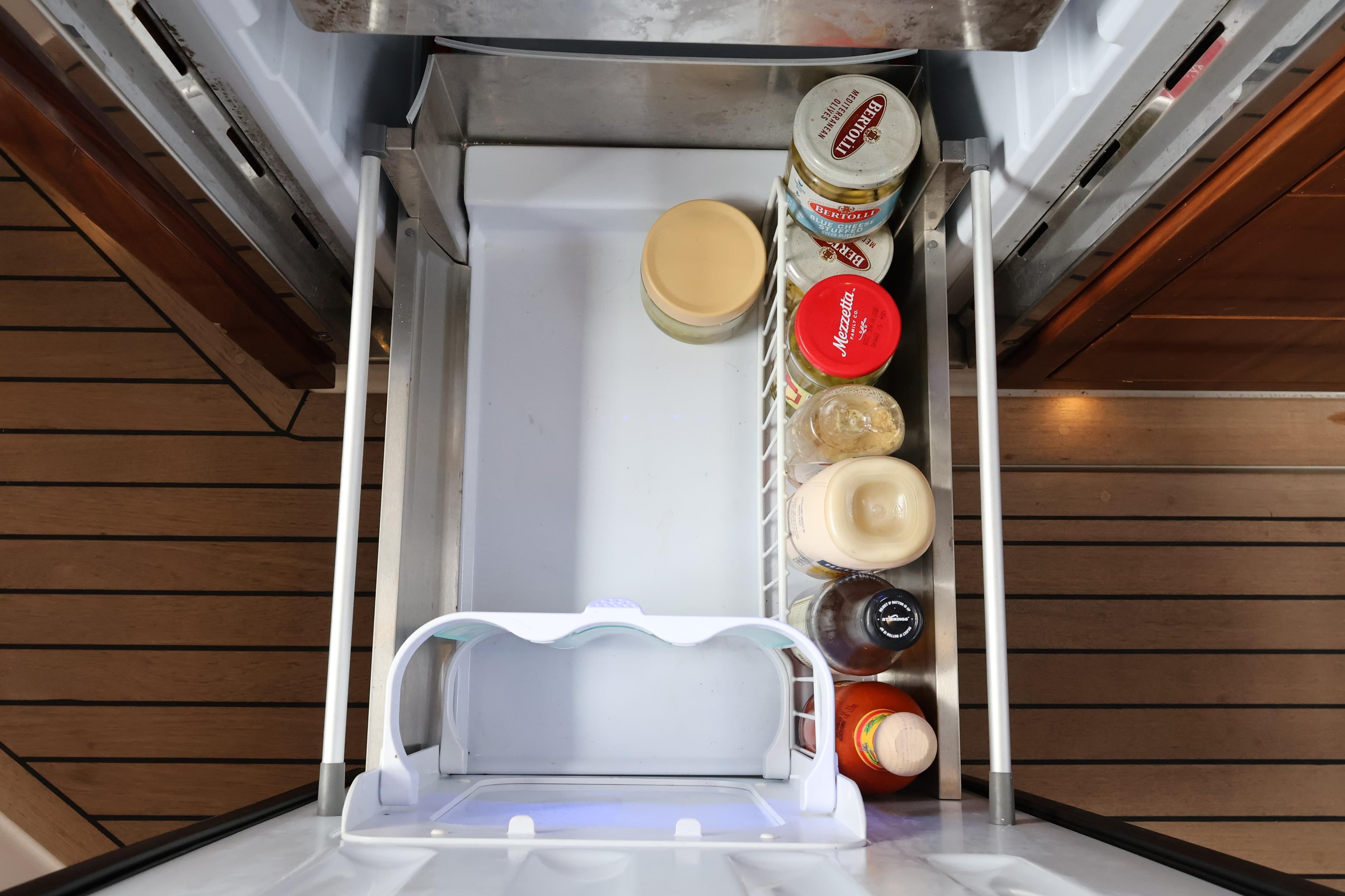 Refrigerator drawer on 2024 Aquador 300 HT yacht with condiments and wooden flooring.