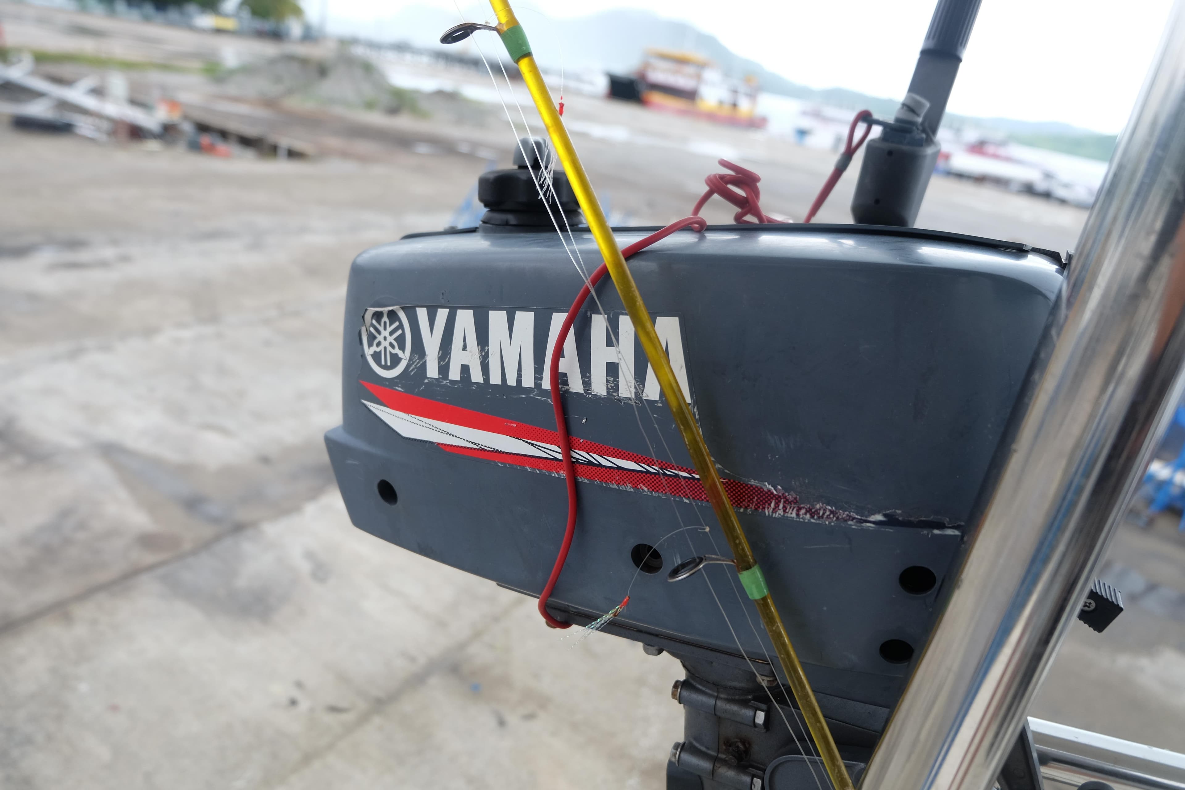 Outboard motor with Yamaha branding, featuring a fishing rod, on a dockside setting.