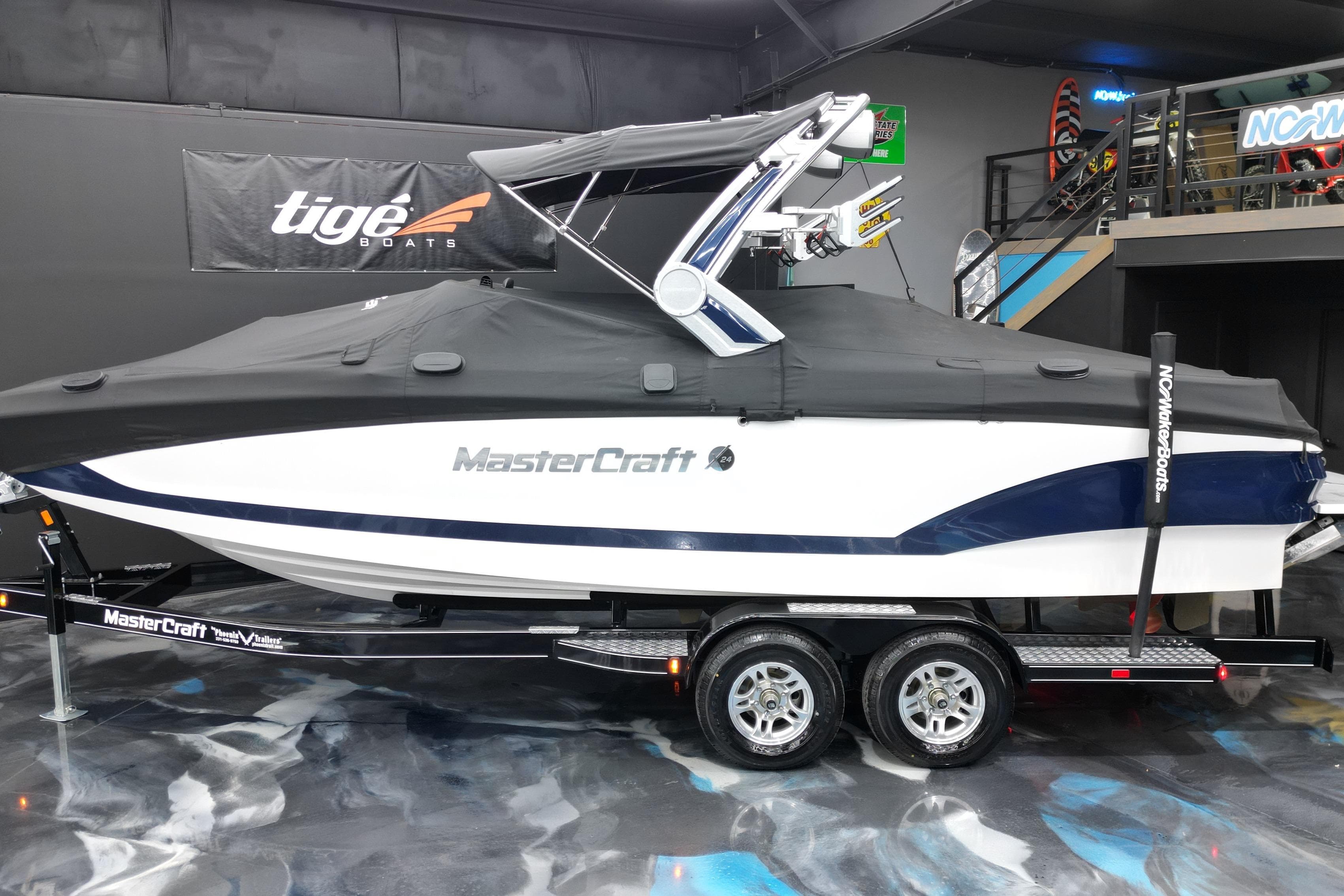 2023 MasterCraft X24 boat on trailer, covered, in showroom setting.