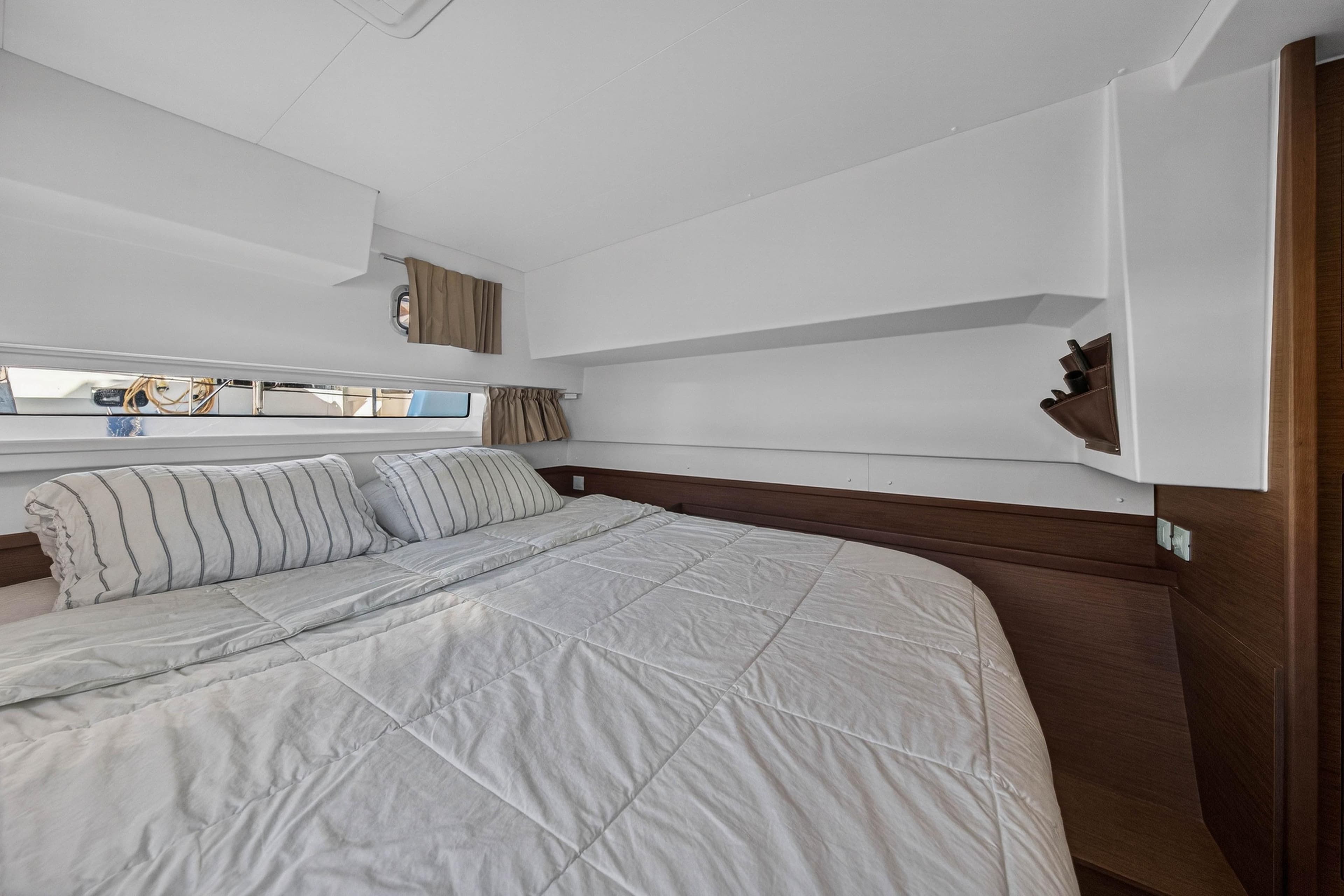 Interior cabin of 2019 Lagoon 42 catamaran with cozy bed and striped pillows.