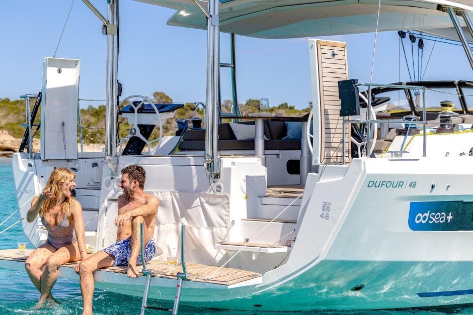 Couple relaxing on a 2026 Dufour 48 yacht, enjoying sunny weather and clear waters.