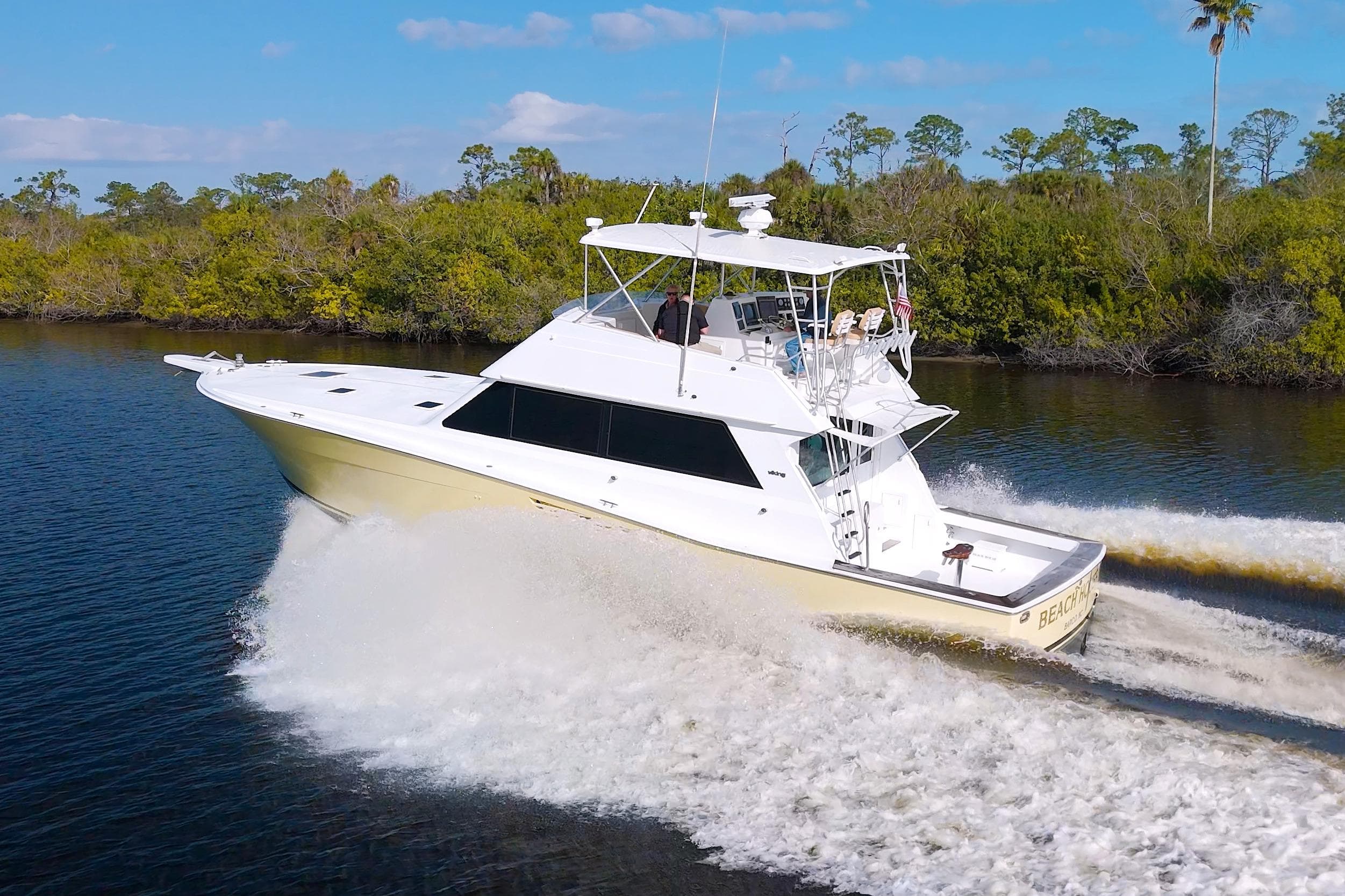1990 Viking 53 Convertible yacht cruising on a scenic waterway with lush greenery.