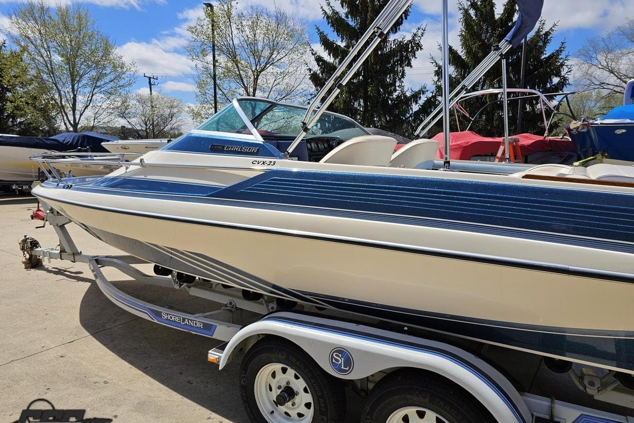 1988 Glastron/Carlson CVX-23 boat on trailer, parked outdoors under blue sky.