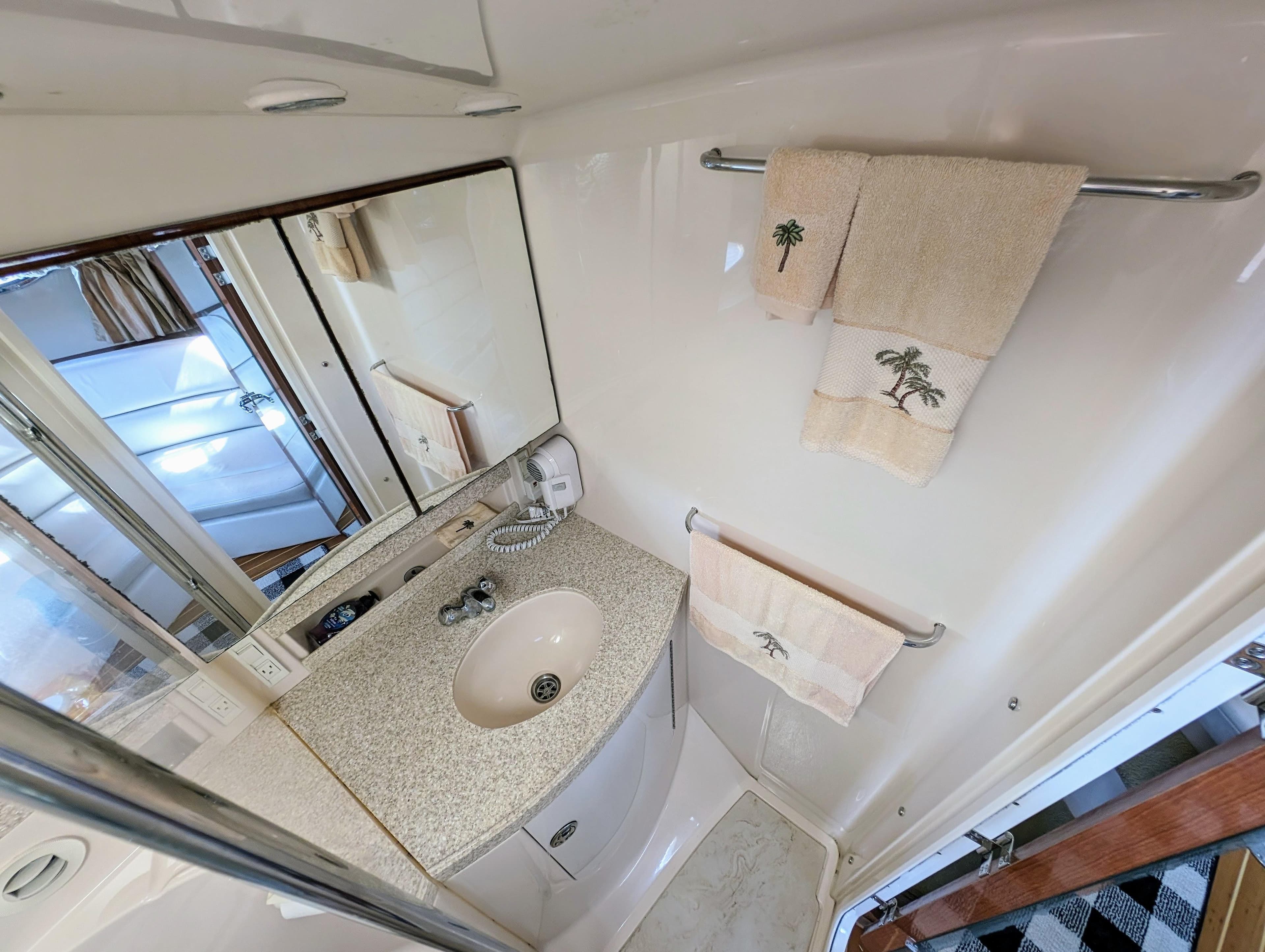 Bathroom interior of 2005 Regal 3560 yacht with sink, mirror, and palm-themed towels.