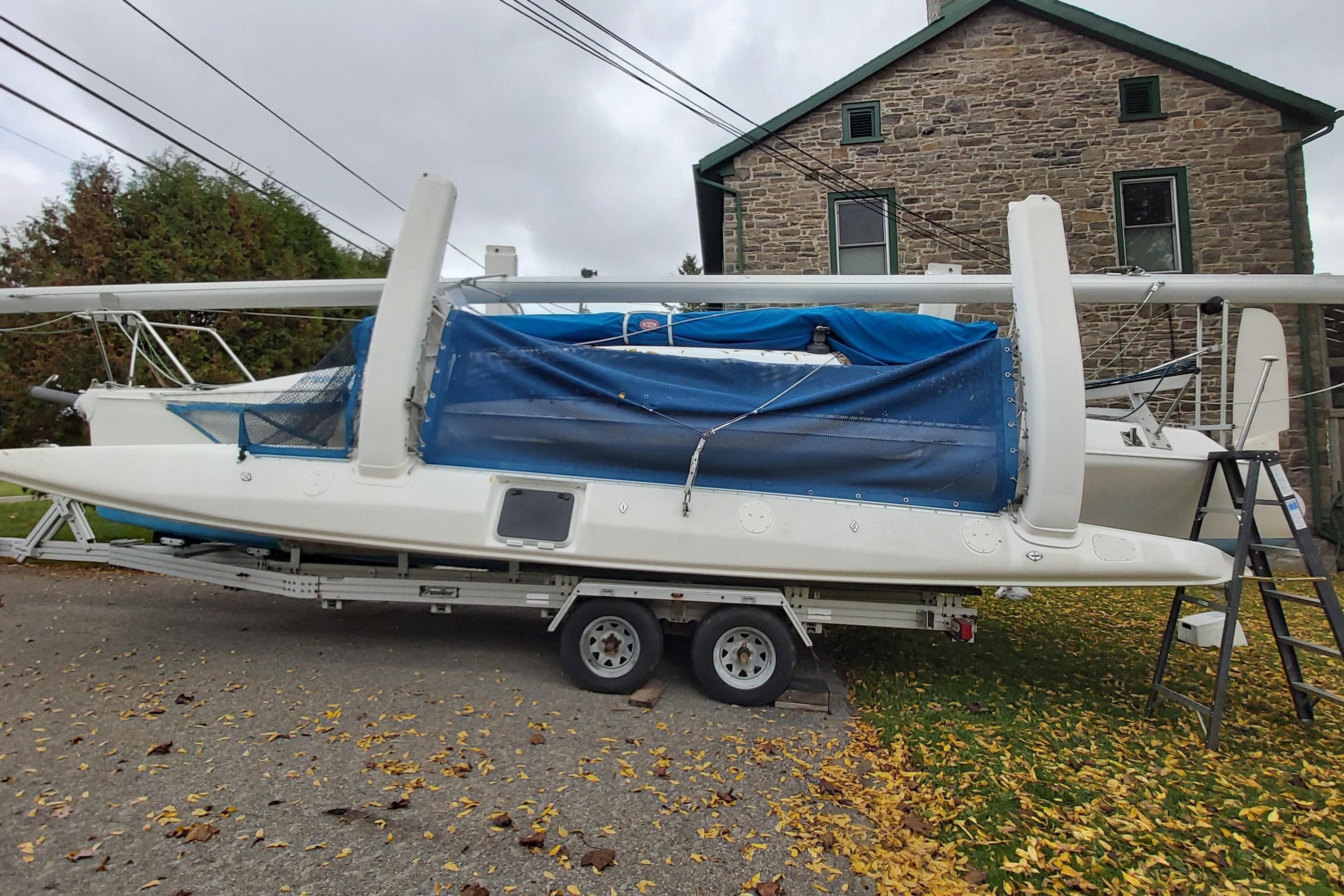 2000 Farrier 31 sailboat on trailer, covered with blue tarp, parked near stone building.