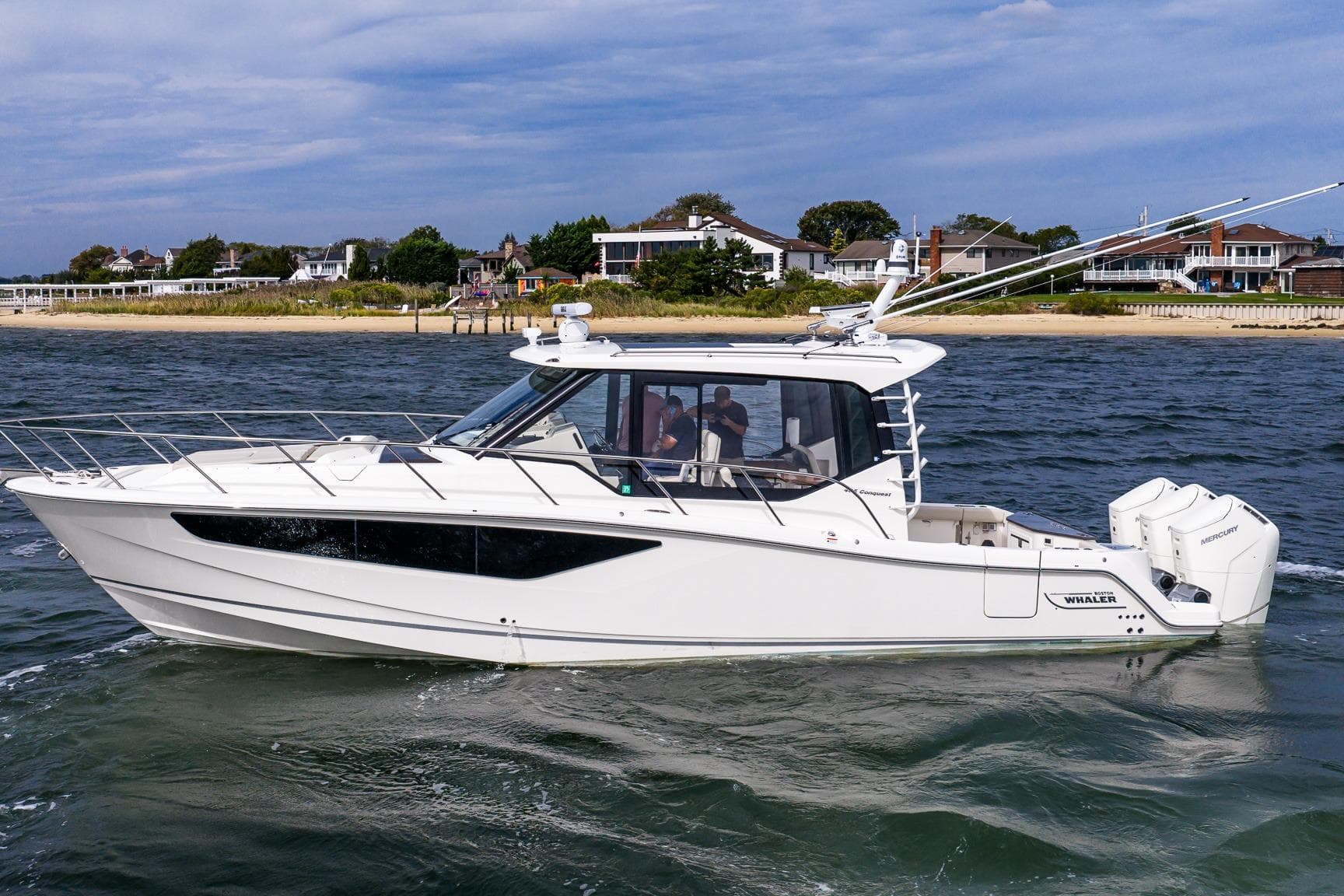 2024 Boston Whaler 405 Conquest cruising on water near coastal homes.