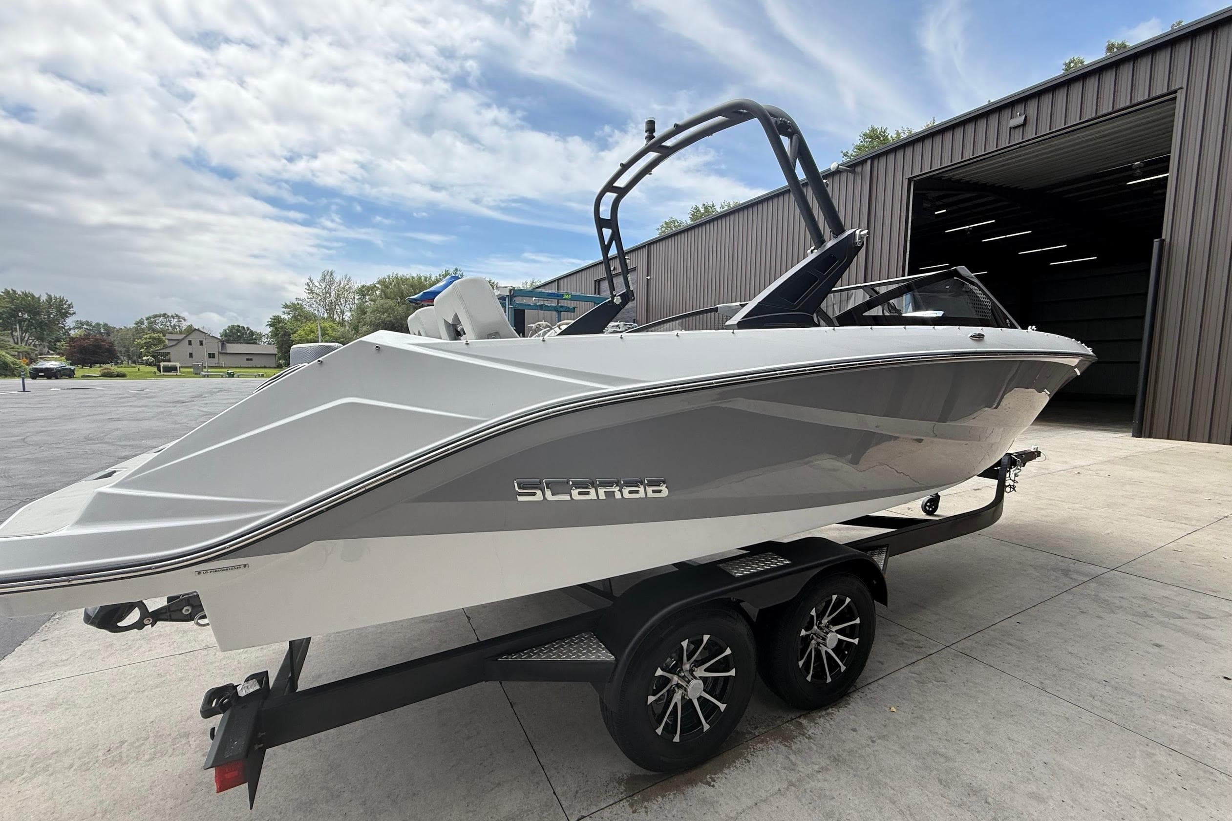 2026 Scarab 235 SE boat on trailer, parked outside a large garage.