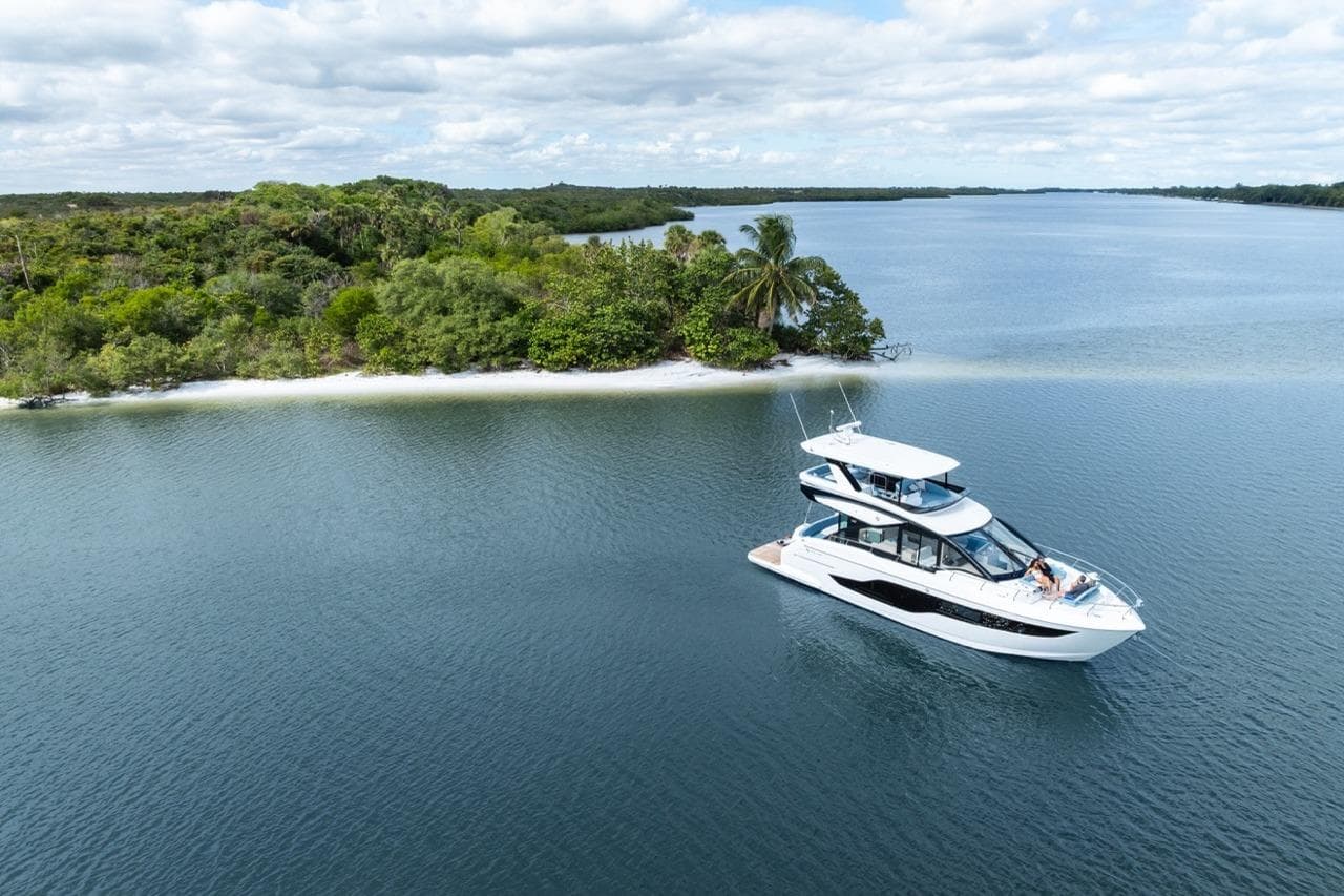Luxurious 2026 Cruisers Yachts 50 Fly cruising near a lush, tropical island.
