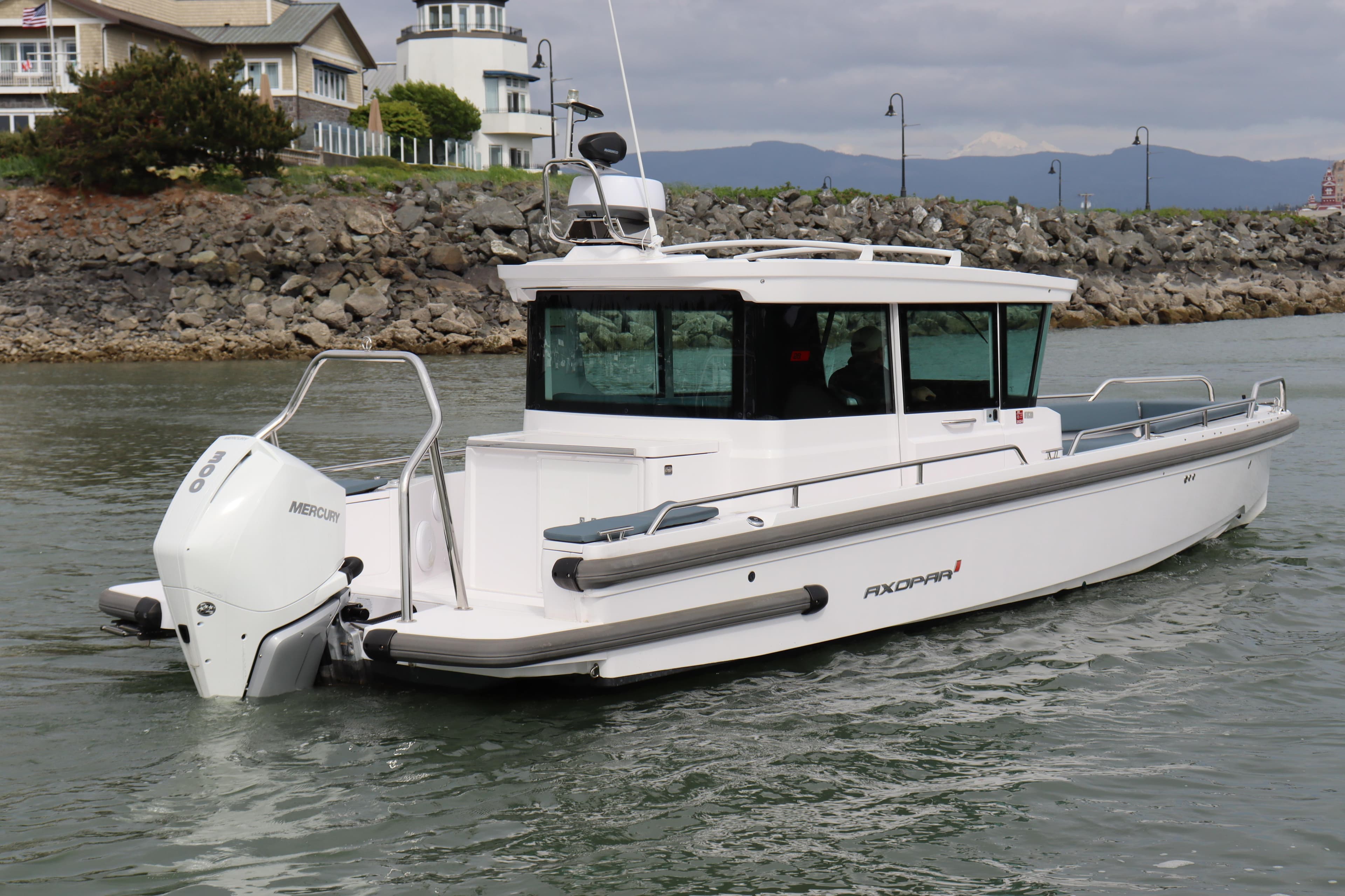2022 Axopar 28 Cabin boat cruising near rocky shoreline with lighthouse in background.