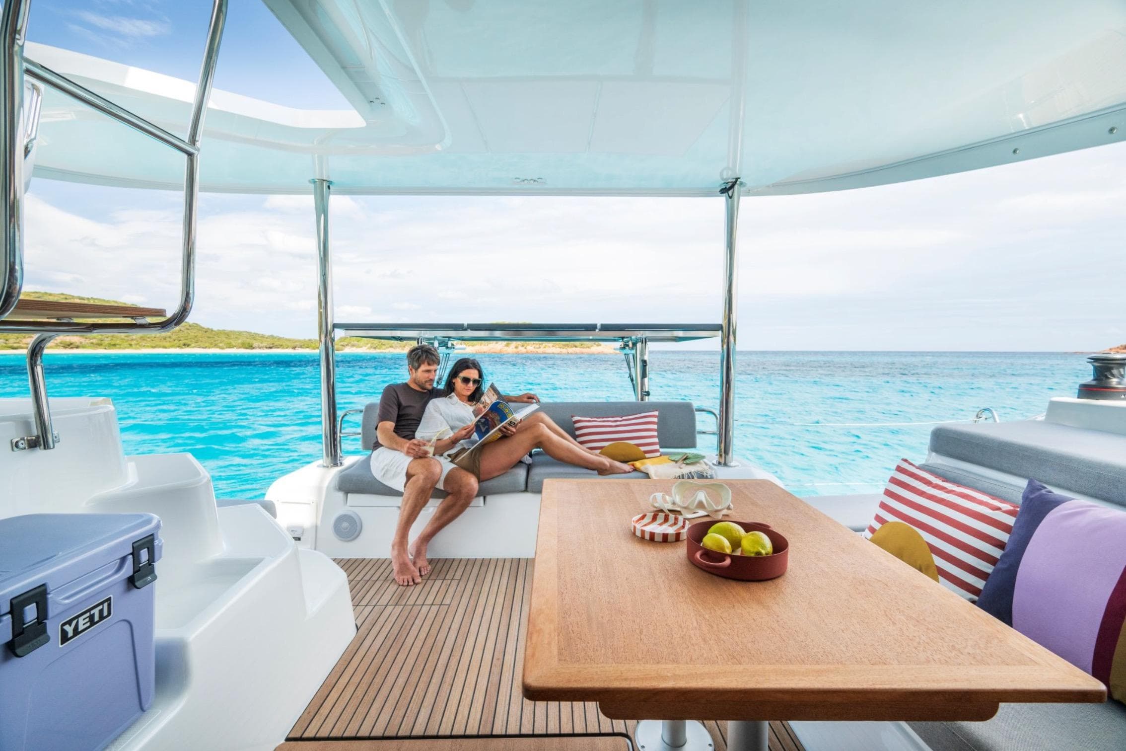 Couple relaxing on Lagoon 38 catamaran, 2026 model, with ocean view and cozy seating.