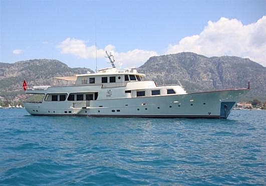 1960 Custom Clelands Shipbuilding TSDMY yacht on blue water with mountainous backdrop.