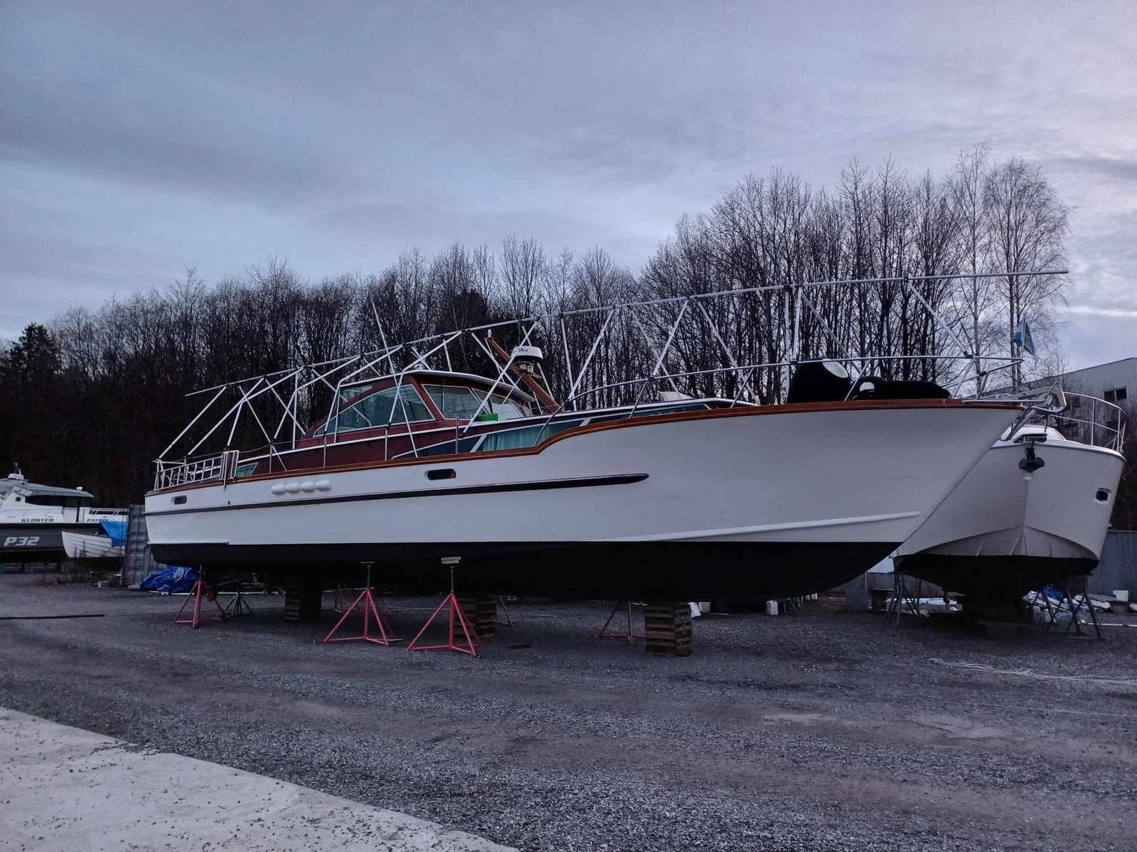 1967 Custom Comtesse boat on stands, surrounded by trees and overcast sky.