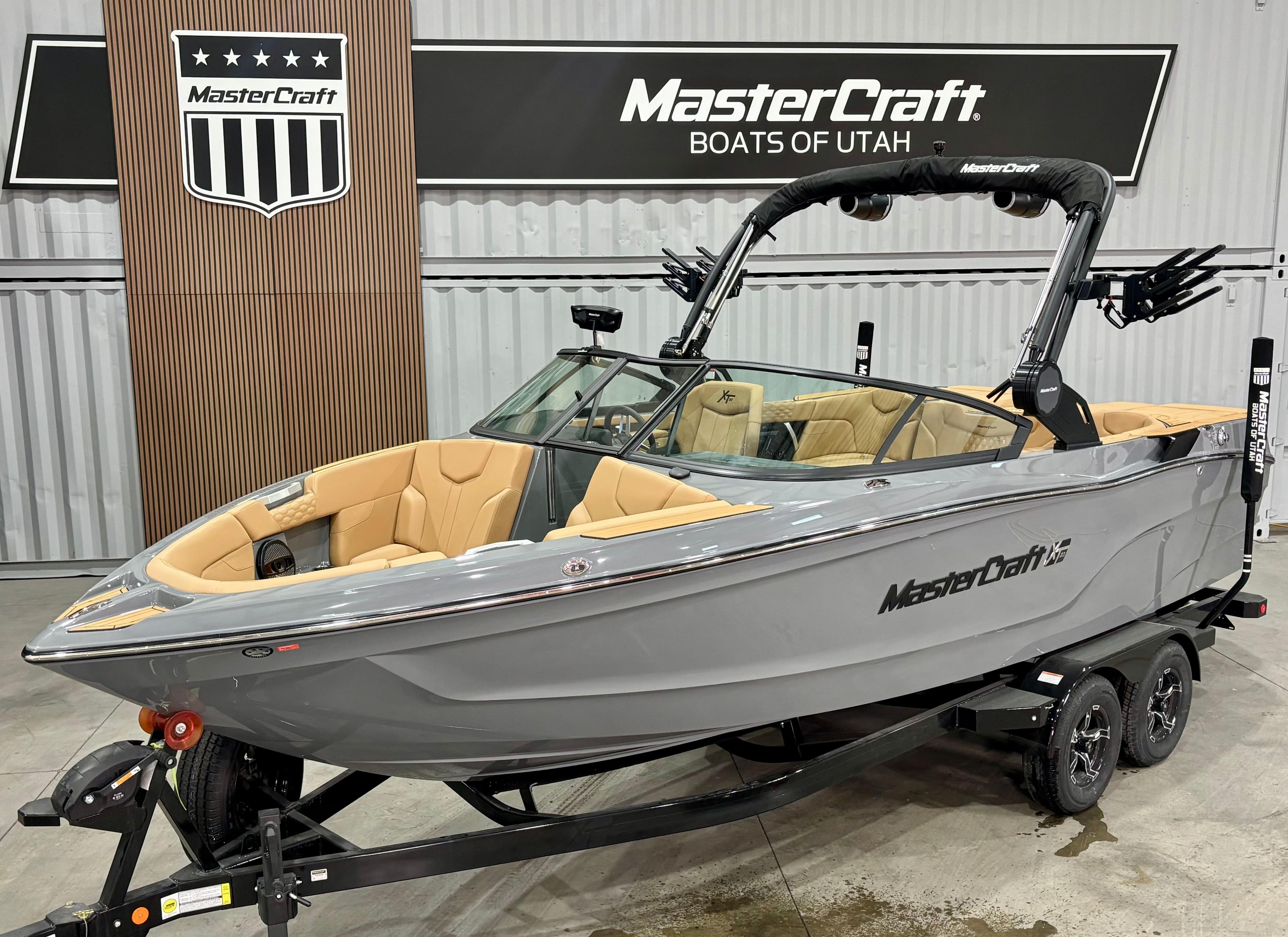 2025 MasterCraft XT23 boat in showroom, gray exterior, tan interior, on trailer.