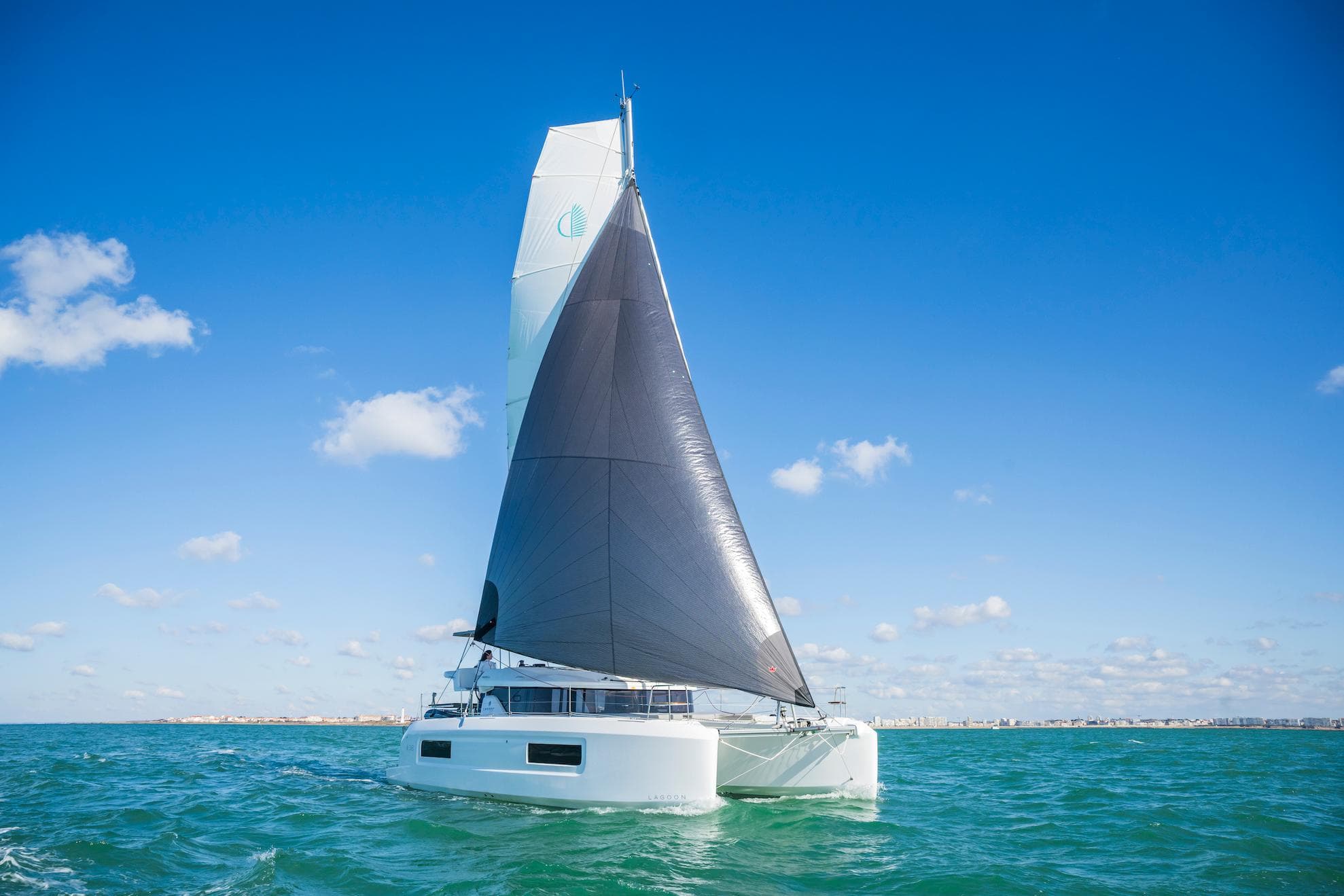 2025 Lagoon 38 catamaran sailing on open sea under clear blue sky.