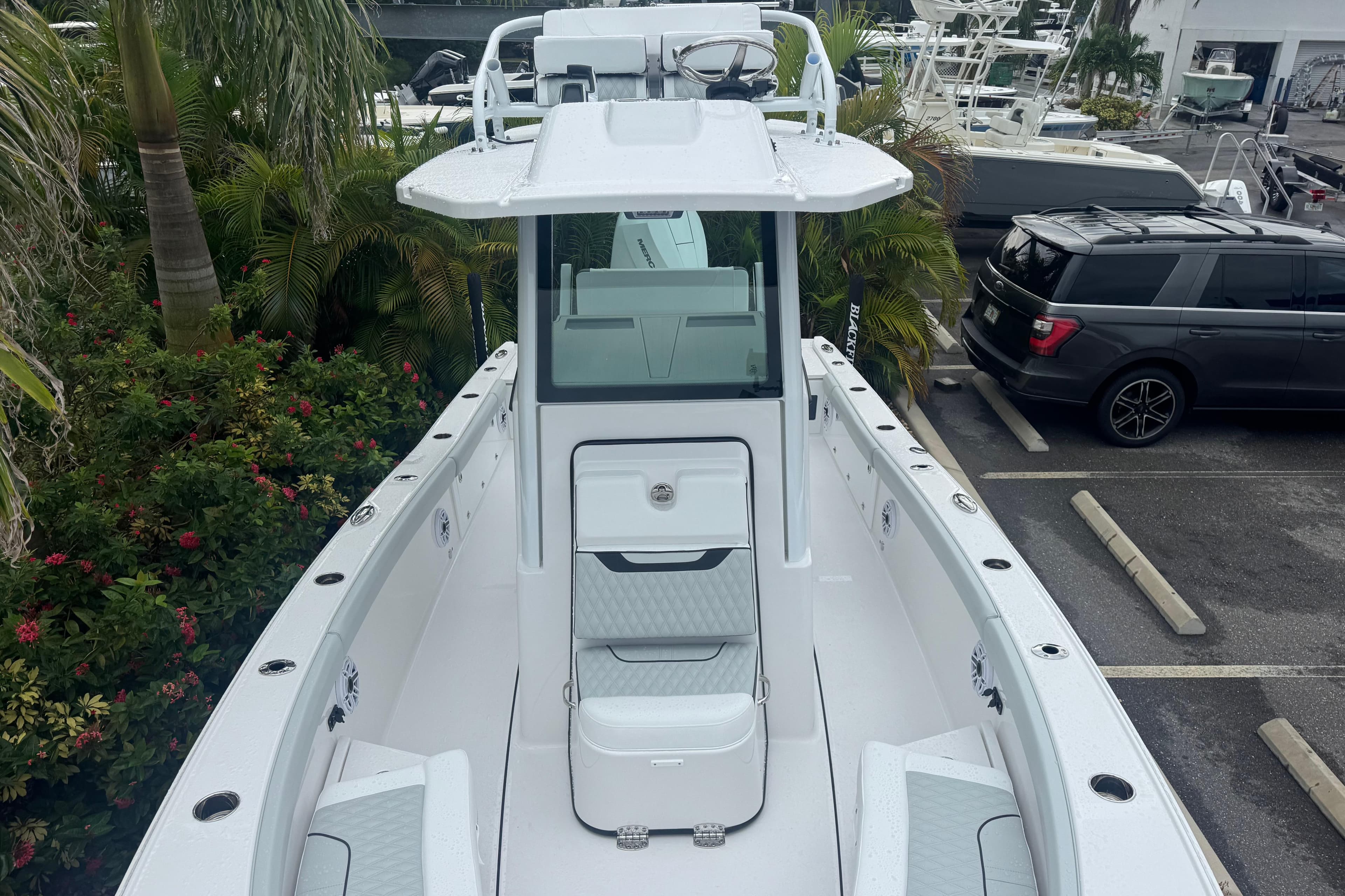 2026 Blackfin 262 HB boat, sleek design, parked near lush greenery and vehicles.