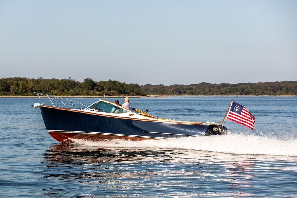 2003 Hinckley T29R boat cruising on a calm lake with American flag.