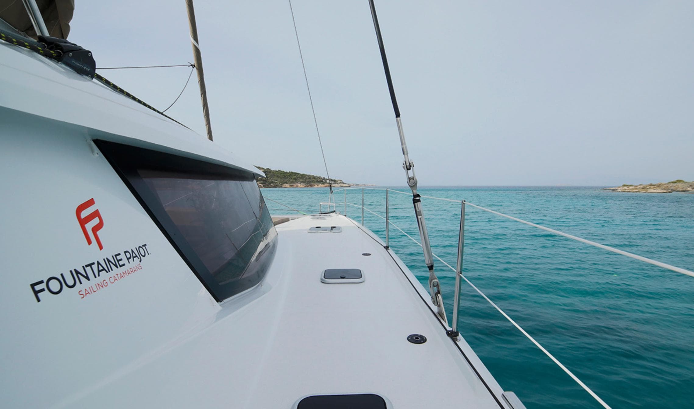 2016 Fountaine Pajot SABA 50 sailing on turquoise waters near a rocky coastline.