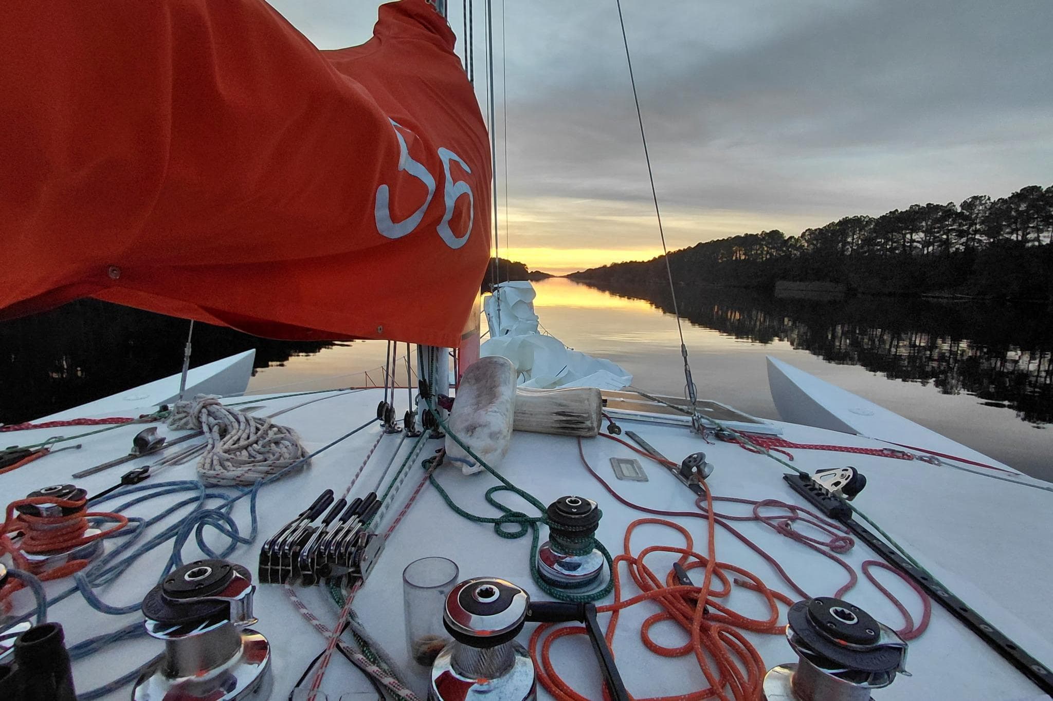 Sailboat deck at sunset, Newick Native 1979, with vibrant orange sail and ropes.
