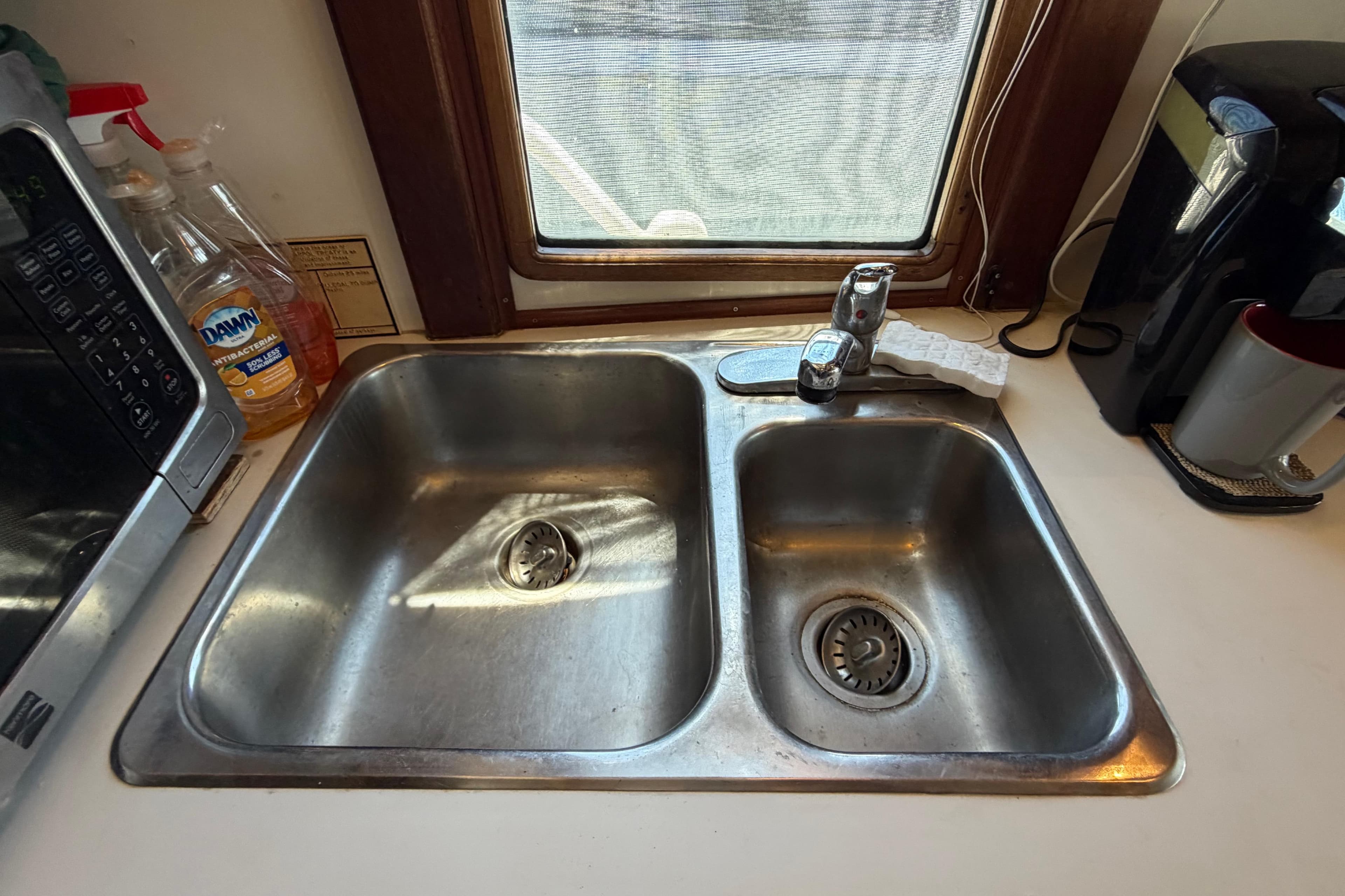 Stainless steel double sink in a 1985 Gozzard PILGRIM kitchen with cleaning supplies.
