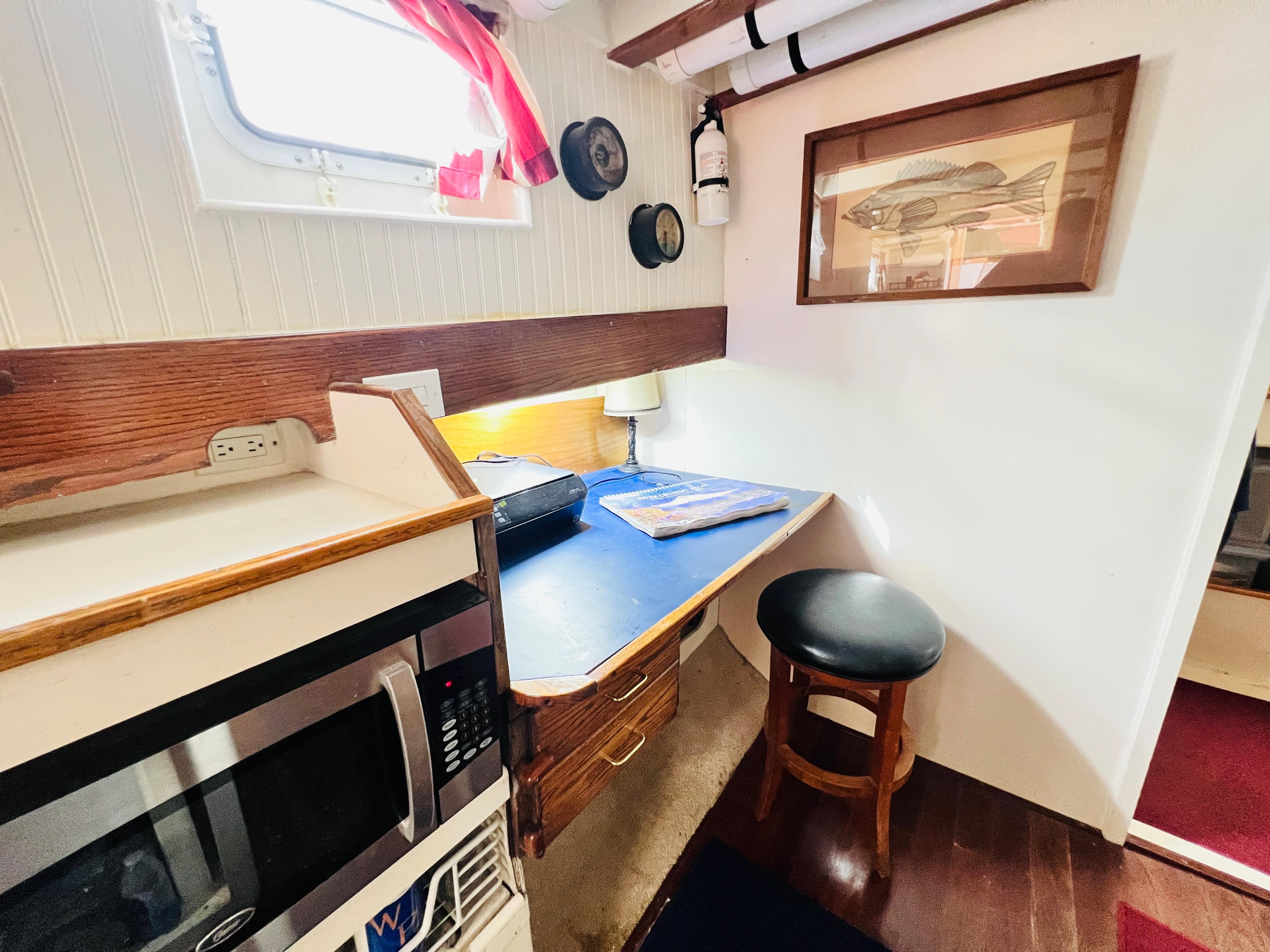Cozy cabin interior of 1955 Colin Archer 42 sailboat with desk, microwave, and porthole window.