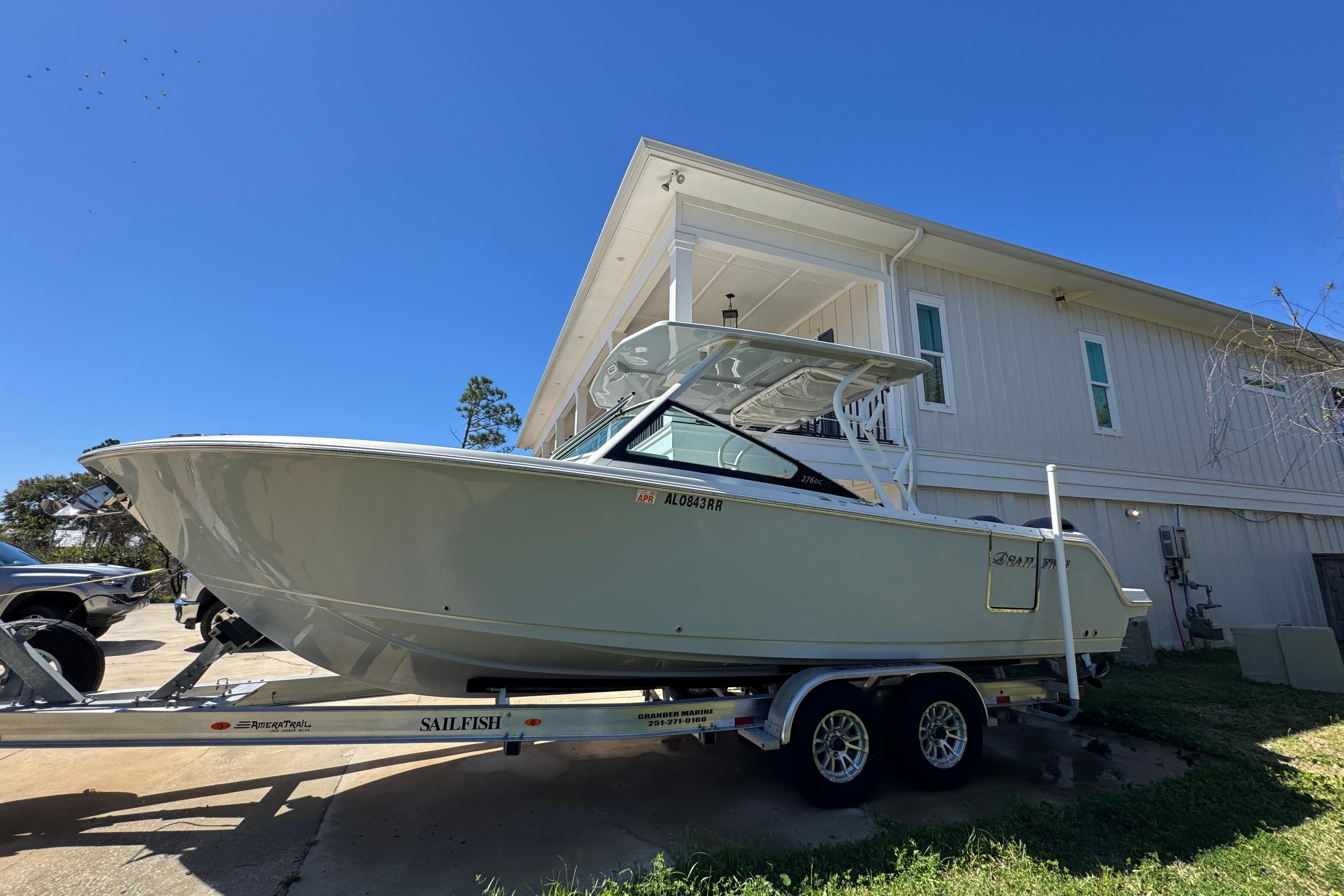 2022 Sailfish 276 DC boat on trailer, parked beside a house under clear blue sky.