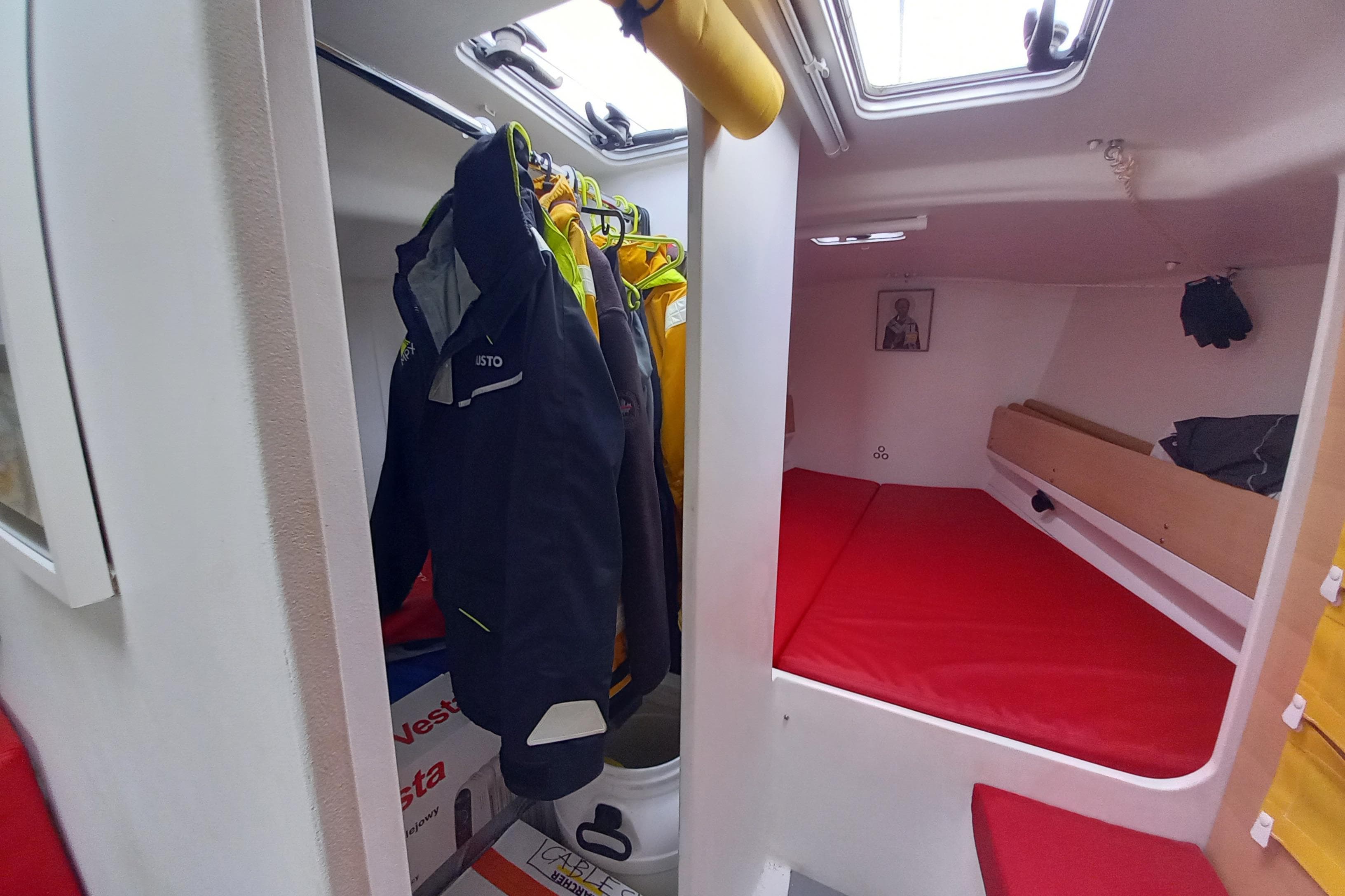 Interior of 2017 Pogo 12.50 sailboat with red bedding and hanging jackets.