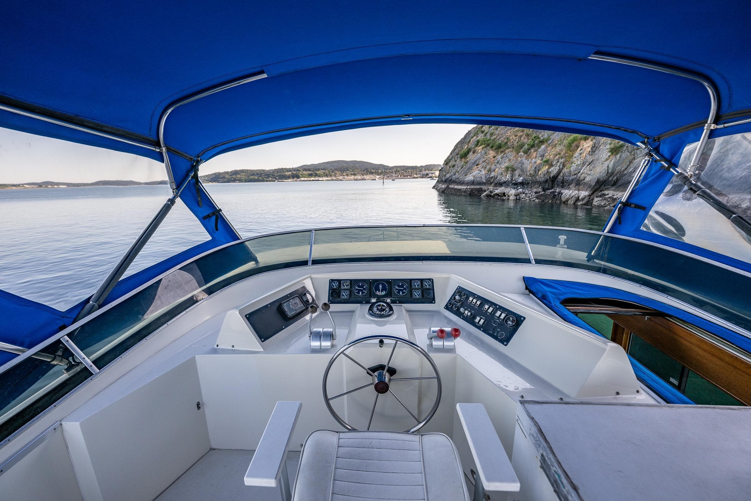 Cockpit view of 1989 Nordic 52 boat with blue canopy, scenic coastal backdrop.