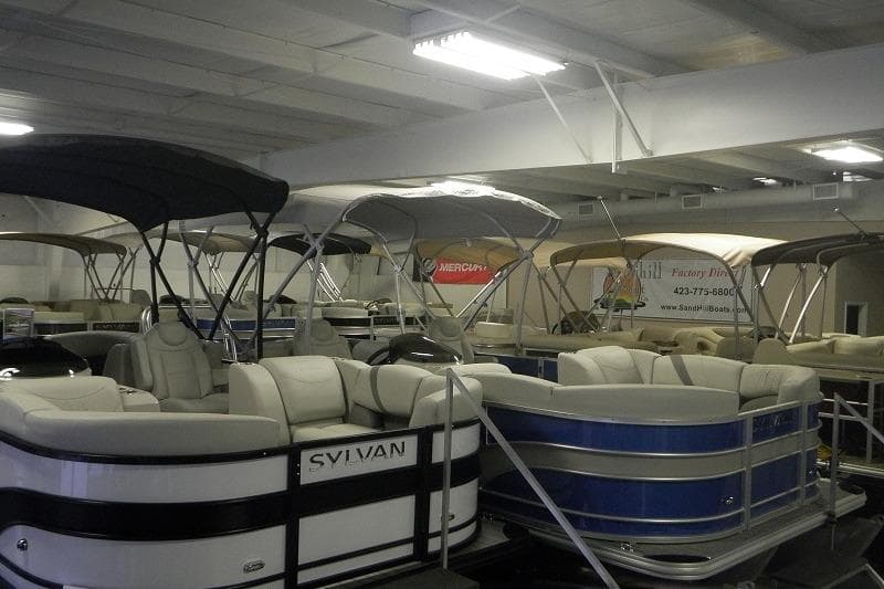 Indoor showroom displaying various pontoon boats, including a 2026 SunChaser Vista 20 CRB model.