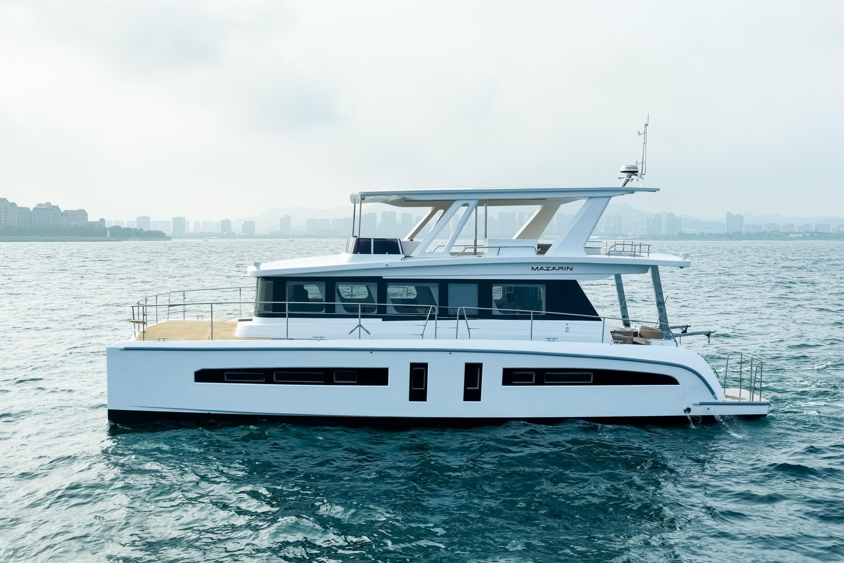 2025 Mazarin 55 Catamaran Diesel cruising on open water, city skyline in background.