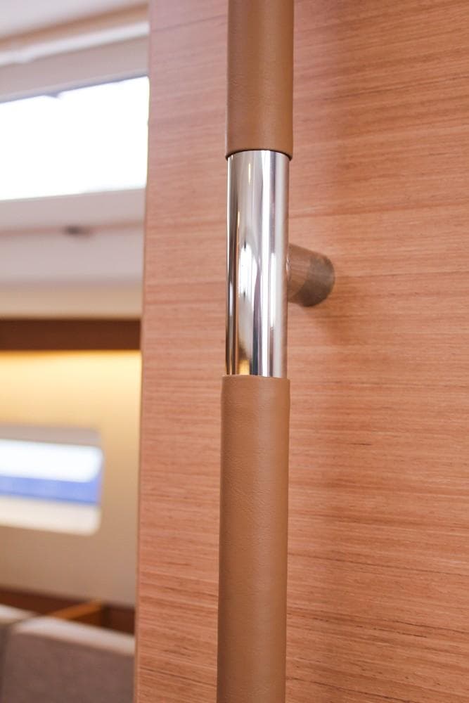 Interior detail of 2025 Jeanneau Sun Odyssey 440 yacht, featuring a sleek wooden and metal handrail.