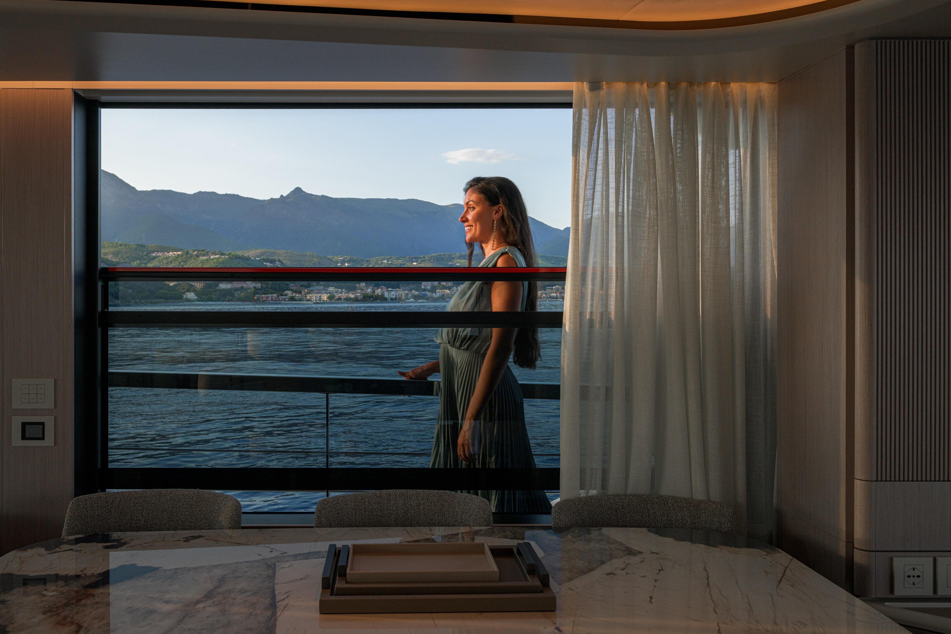 Woman enjoying view from Absolute 62' Navetta yacht, 2026 model, with scenic mountain backdrop.
