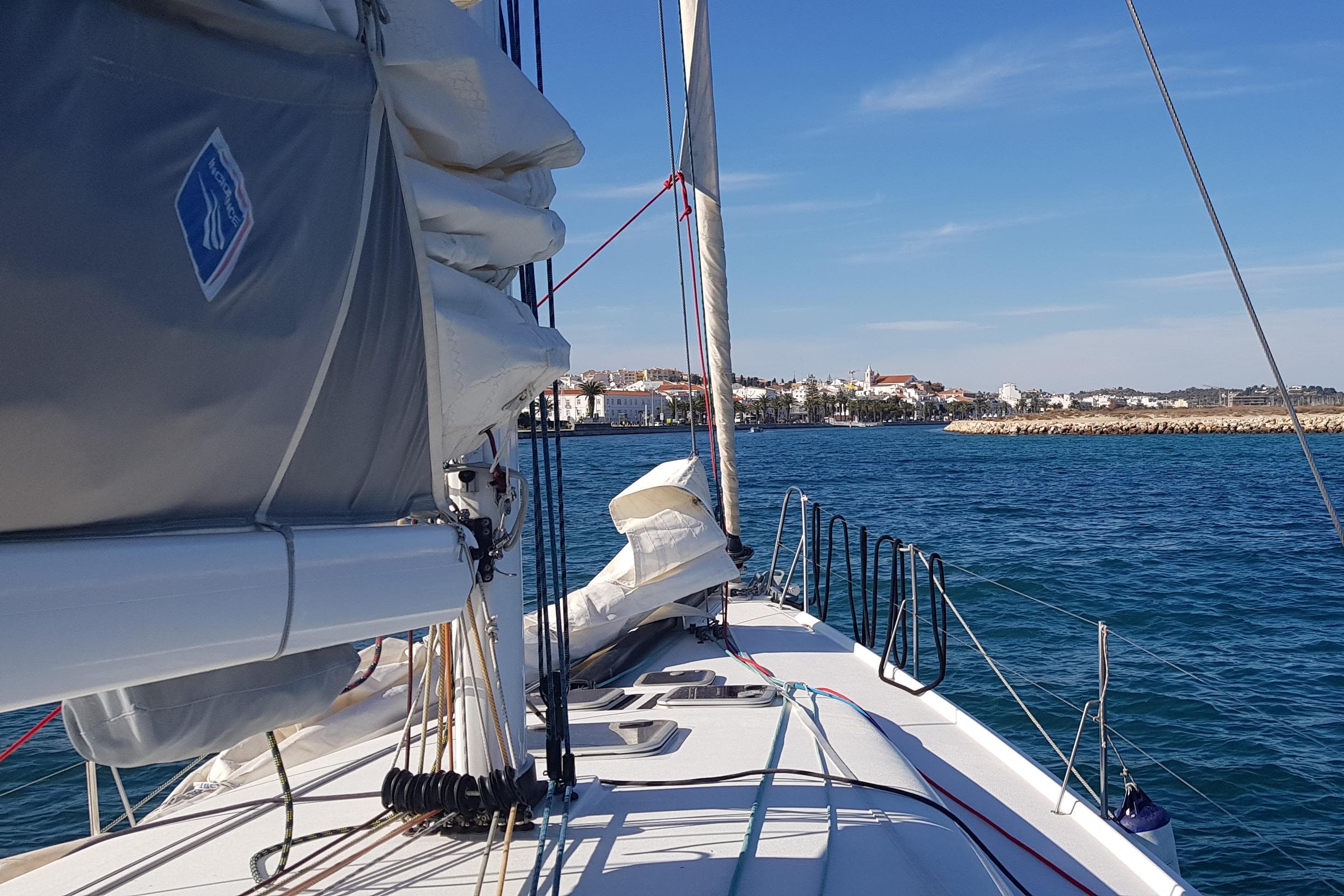 Sailing on a 2017 Pogo 1250 yacht approaching a coastal town under clear blue skies.