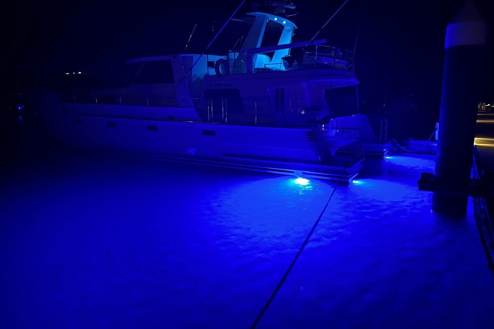 2001 Malcolm Tennant Pachoud Pilothouse Powercat illuminated with blue underwater lights at night.