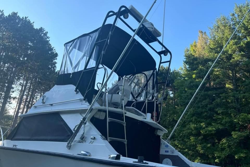 1977 Bertram 28 Flybridge boat with canopy, surrounded by trees under clear blue sky.