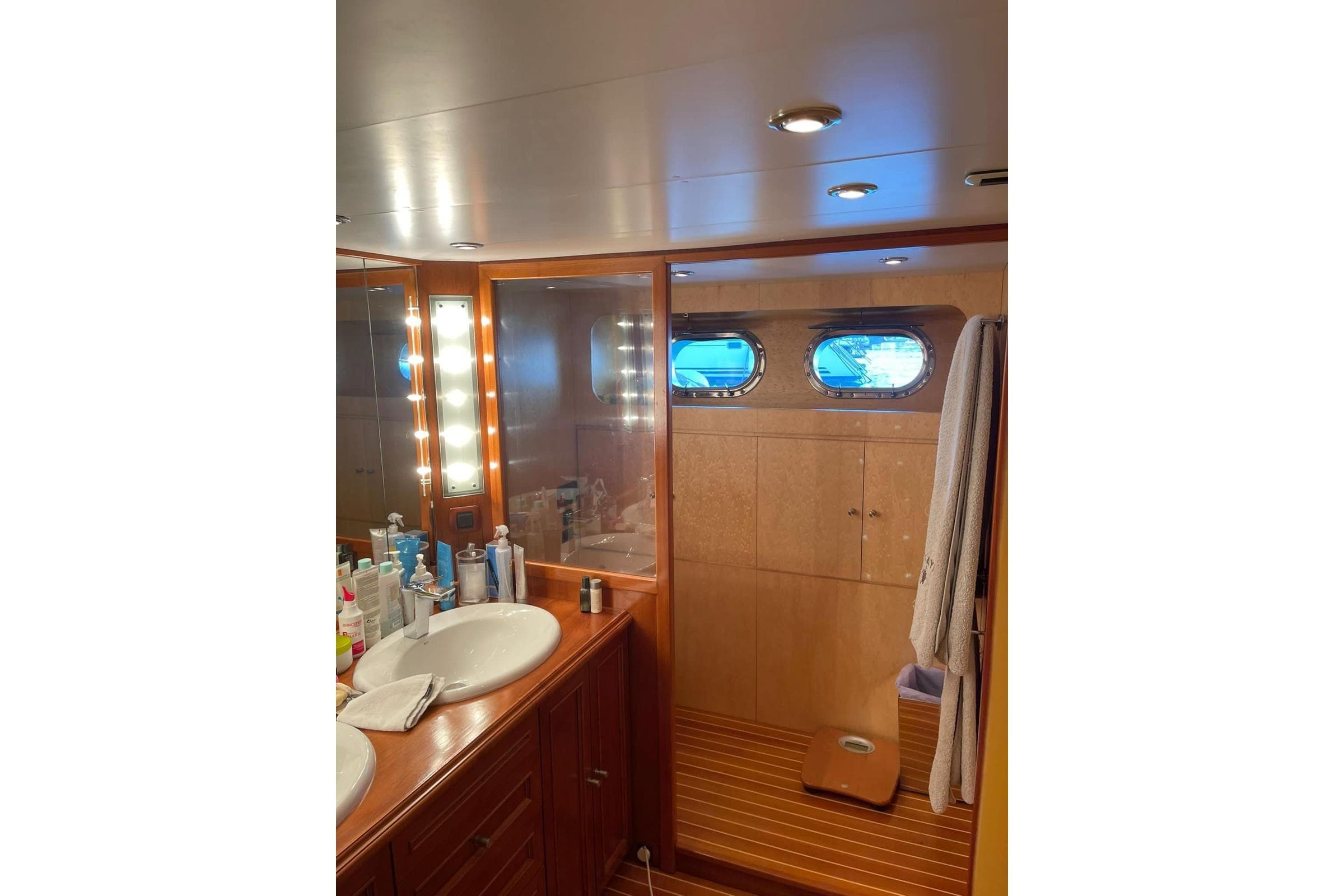 Luxurious bathroom interior of 1985 Astondoa 24 yacht with wooden accents and porthole windows.